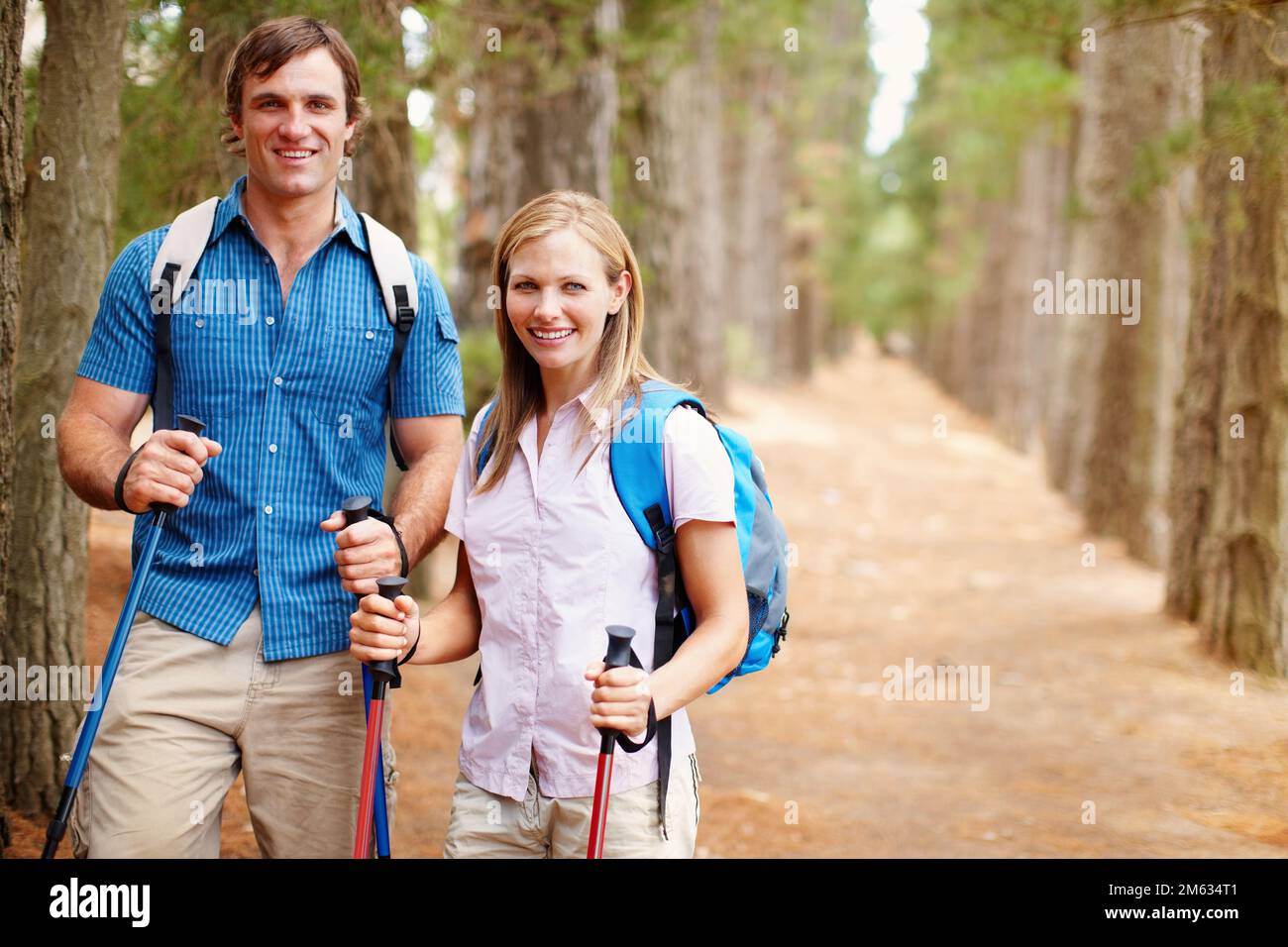 Coppia escursionistica in piedi nel bosco e sorridente. Ritratto di coppia in piedi nel bosco con zaino e pali da trekking e dando un attraente Foto Stock