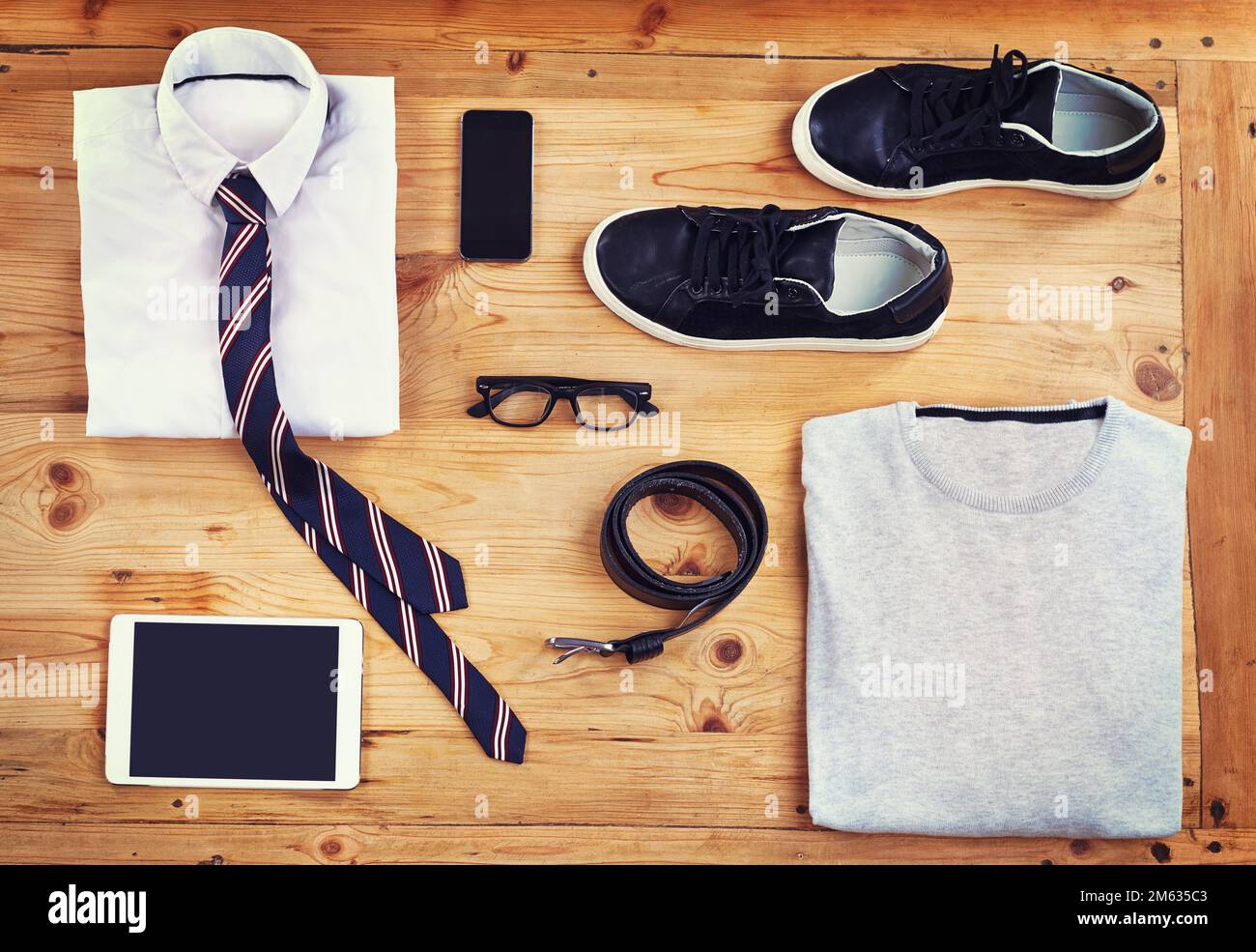 Kit per l'uomo moderno. Inquadratura ad alta angolazione di un outfit elegante e casual con dispositivi digitali disposti su un tavolo di legno. Foto Stock