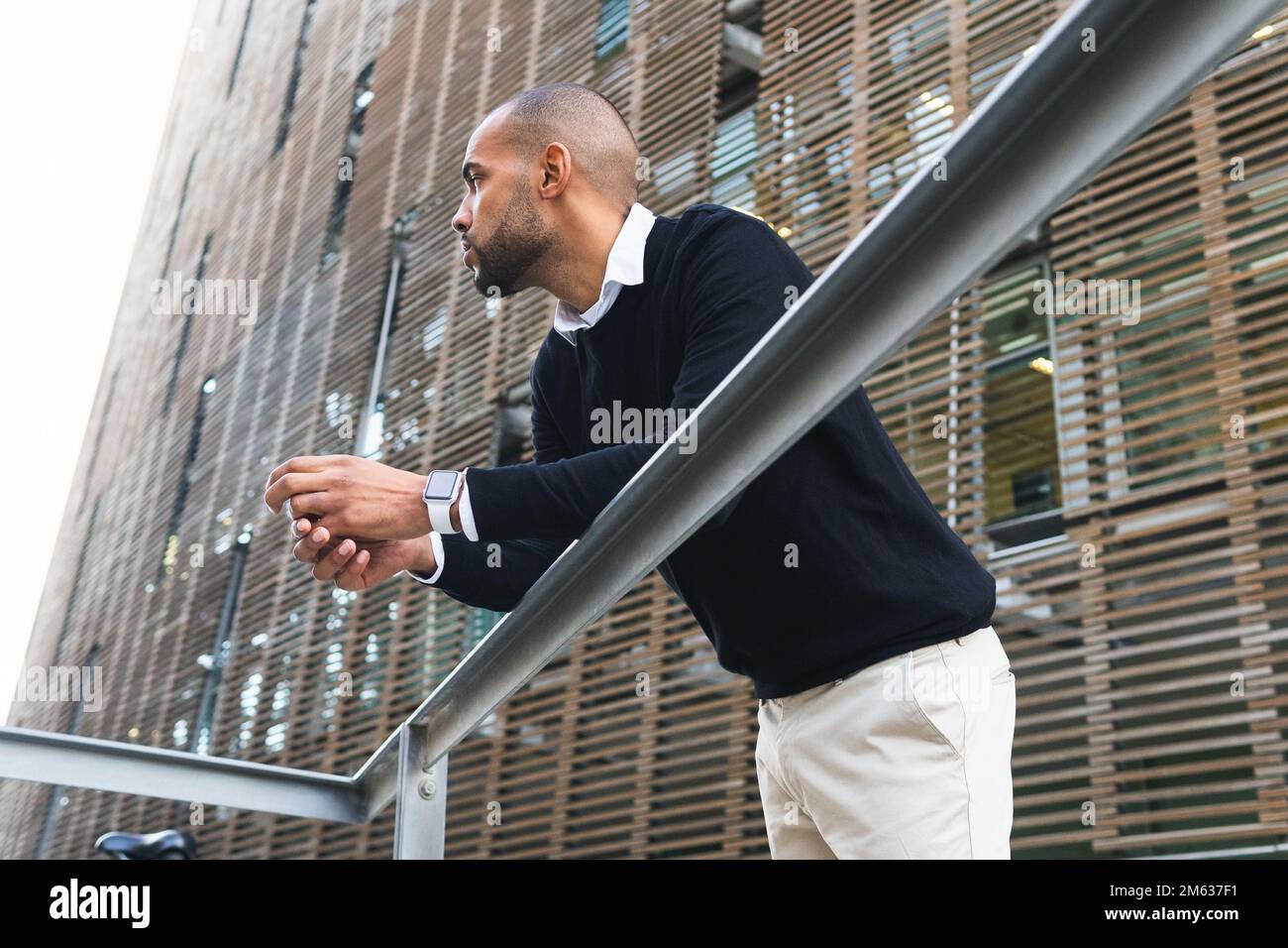 Basso angolo di barbuto nero maschio manager in elegante abito casual in piedi contro moderno edificio di uffici durante la pausa dal lavoro Foto Stock