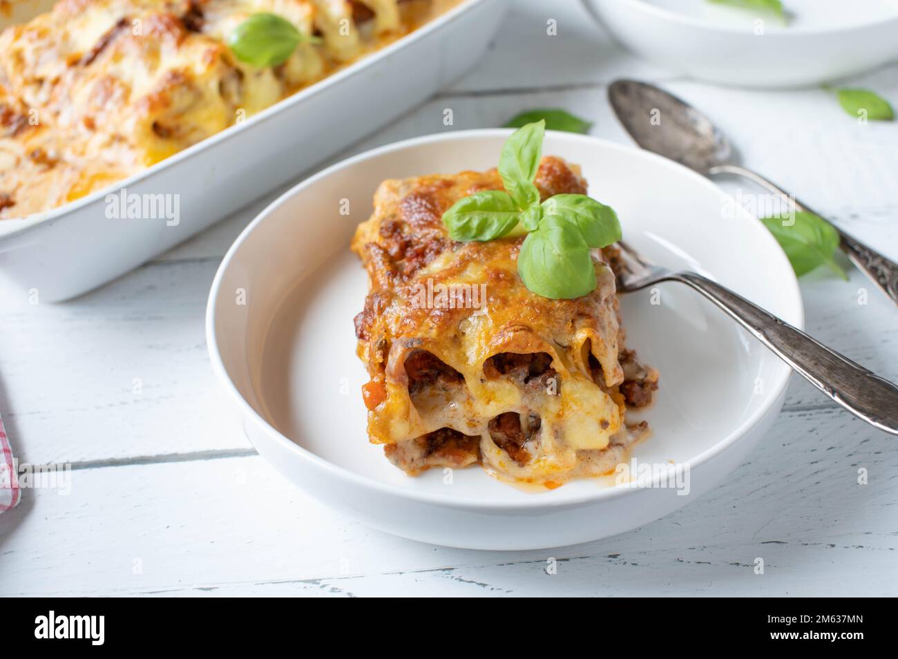 Pezzo di casseruola noodle. Al forno con cannelloni, bolognese e bechamel salsa e mozzarella farcita su sfondo bianco da tavola Foto Stock