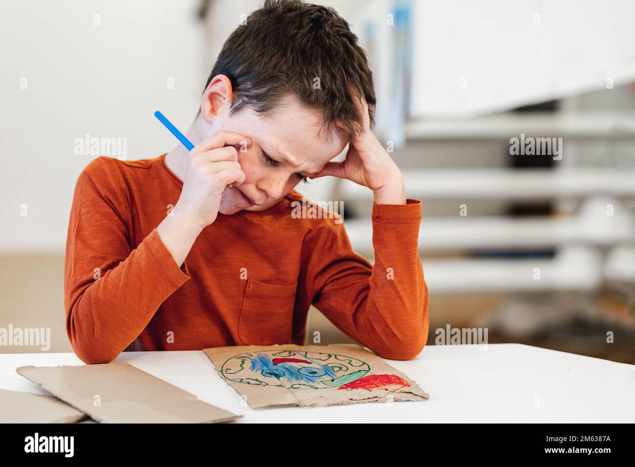 Ragazzo pensivo in abiti casual che toccano la testa e accigliano mentre si siede al tavolo e la creazione di poster ambientale a casa Foto Stock