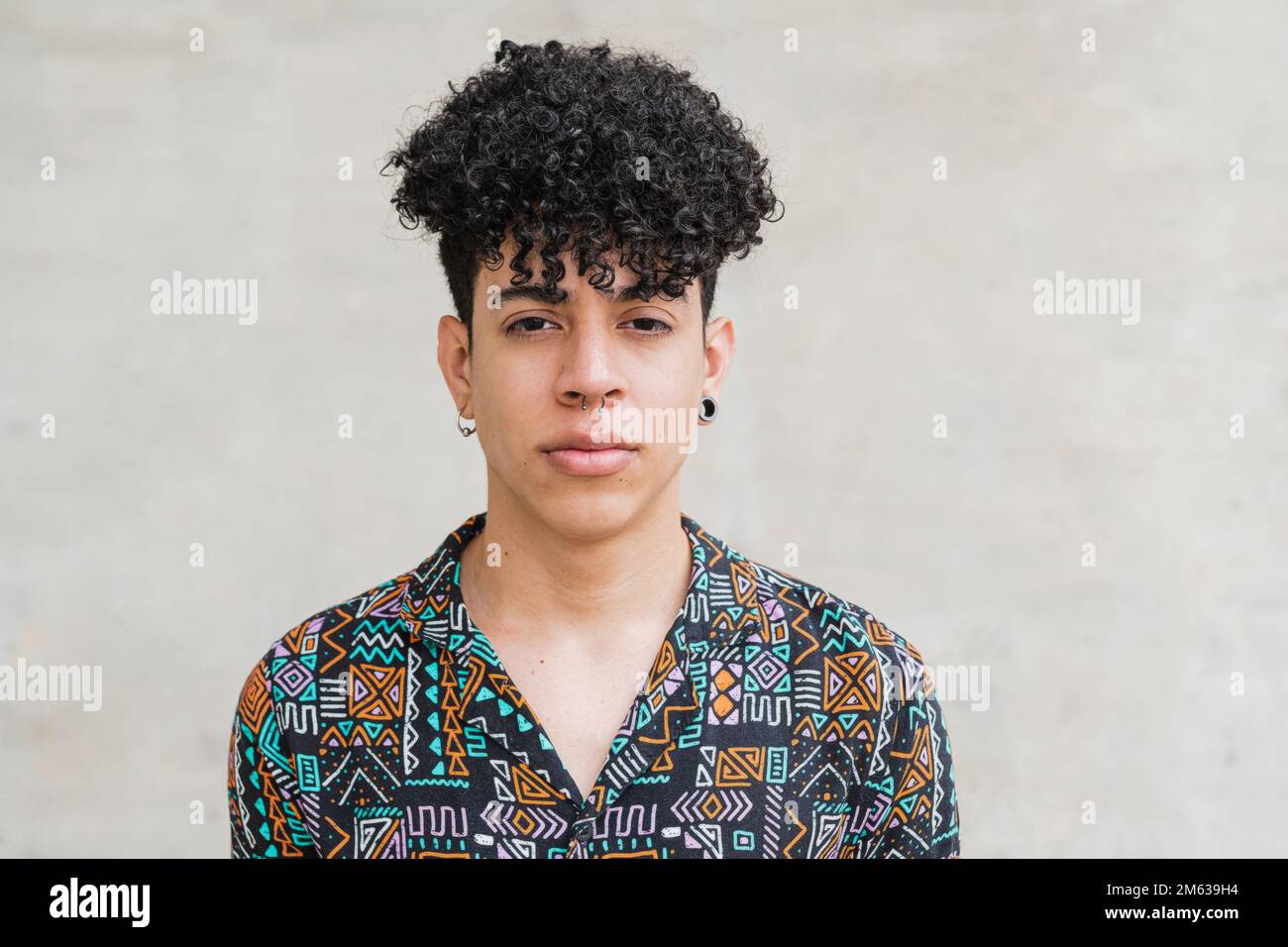 Uomo etnico in camicia e pantaloni con acconciatura afro in piedi contro parete di cemento guardando la macchina fotografica Foto Stock