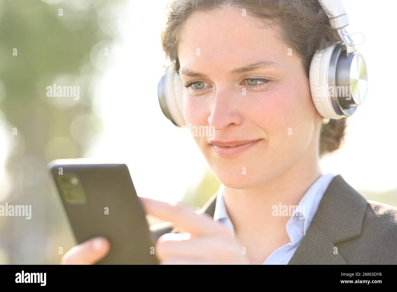 Donna d'affari che indossa cuffie per ascoltare l'audio e controllare il telefono Foto Stock