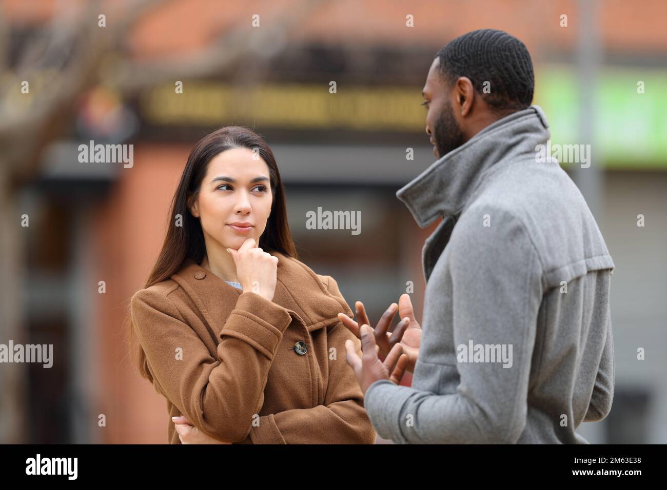 Donna sospetta che ascolta un uomo che parla per strada in inverno Foto Stock