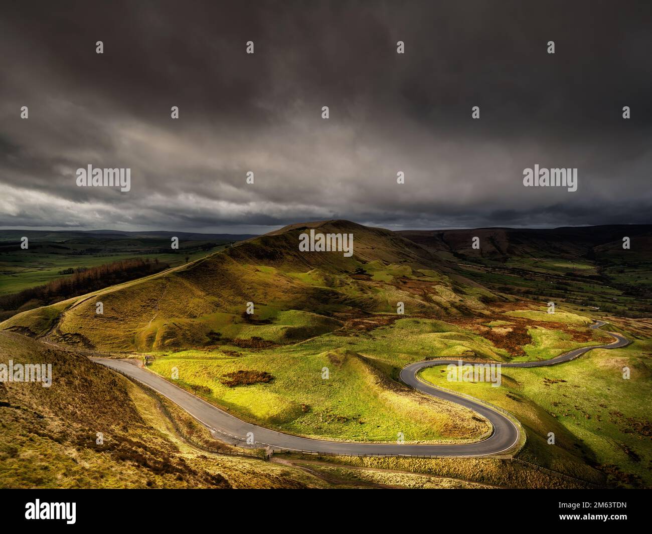 Strada tortuosa attraverso il Peak District, Inghilterra, sotto cieli drammaticamente mutevoli e un tempo malinconico nella rugosa campagna montuosa. Foto Stock