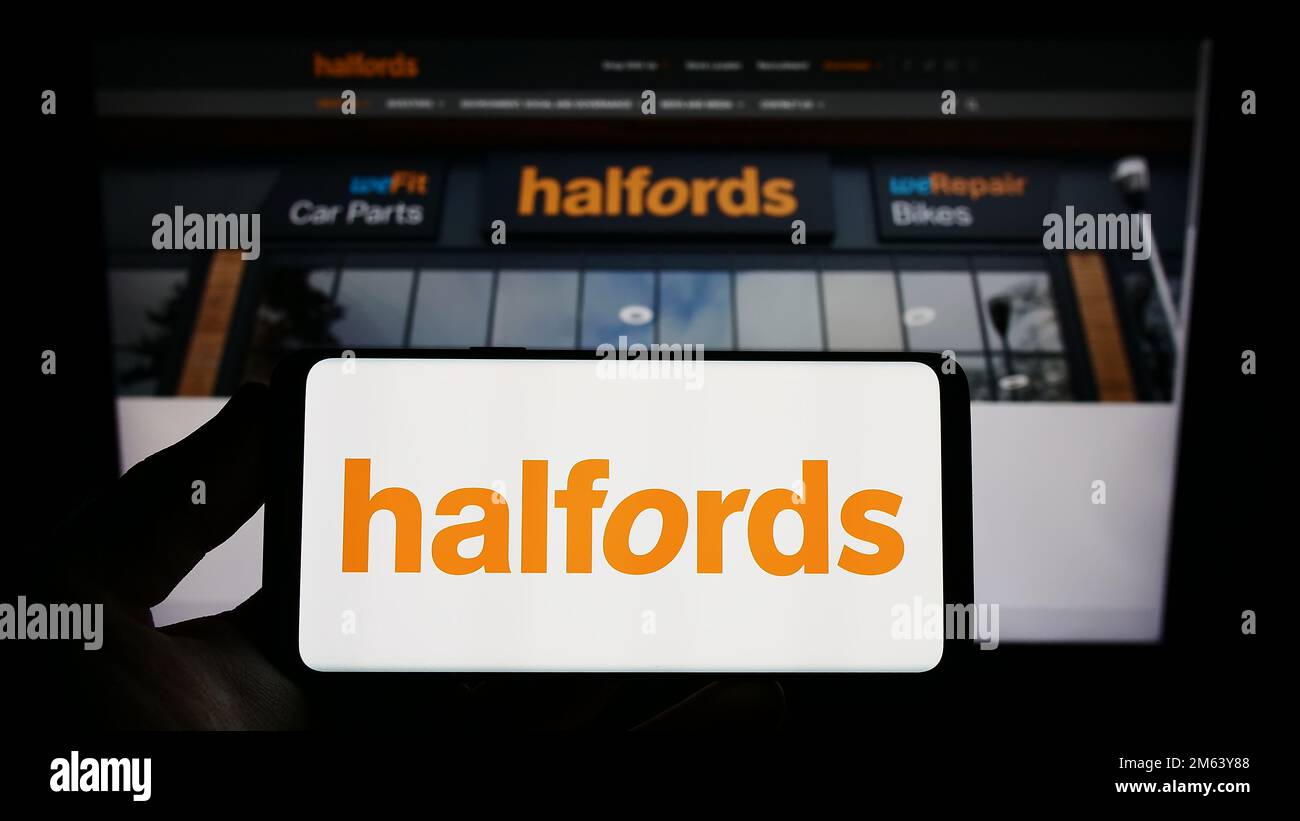 Persona che tiene in mano uno smartphone con il logo della società britannica di vendita al dettaglio Halfords Group plc sullo schermo davanti al sito Web. Messa a fuoco sul display del telefono. Foto Stock