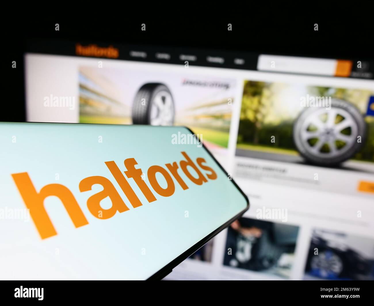 Smartphone con il logo della società di vendita al dettaglio britannica Halfords Group plc sullo schermo di fronte al sito Web aziendale. Messa a fuoco al centro del display del telefono. Foto Stock