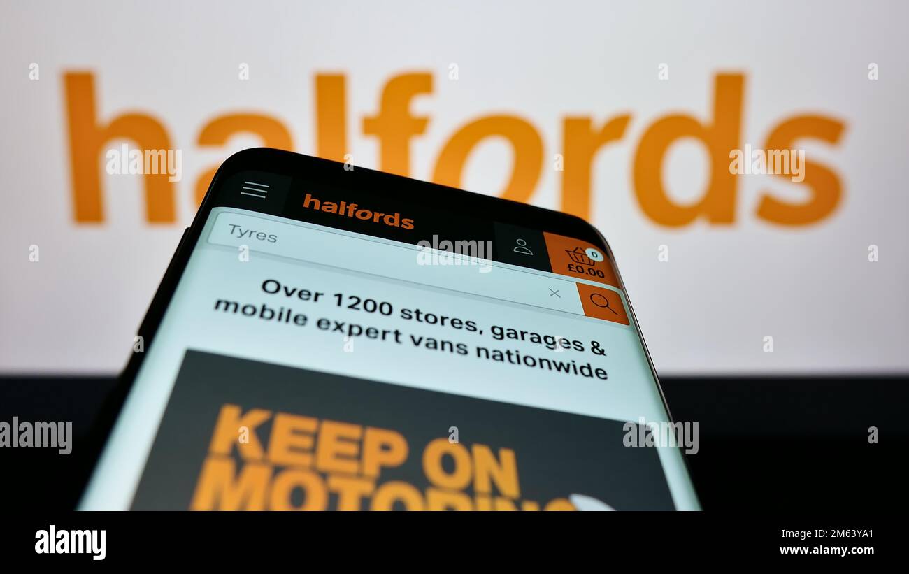 Telefono cellulare con sito web della società britannica di vendita al dettaglio Halfords Group plc sullo schermo di fronte al logo aziendale. Messa a fuoco in alto a sinistra del display del telefono. Foto Stock