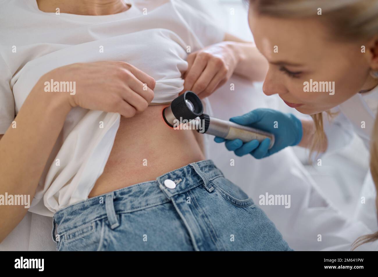 Dermatologo che esamina il paziente con lente d'ingrandimento in clinica Foto Stock