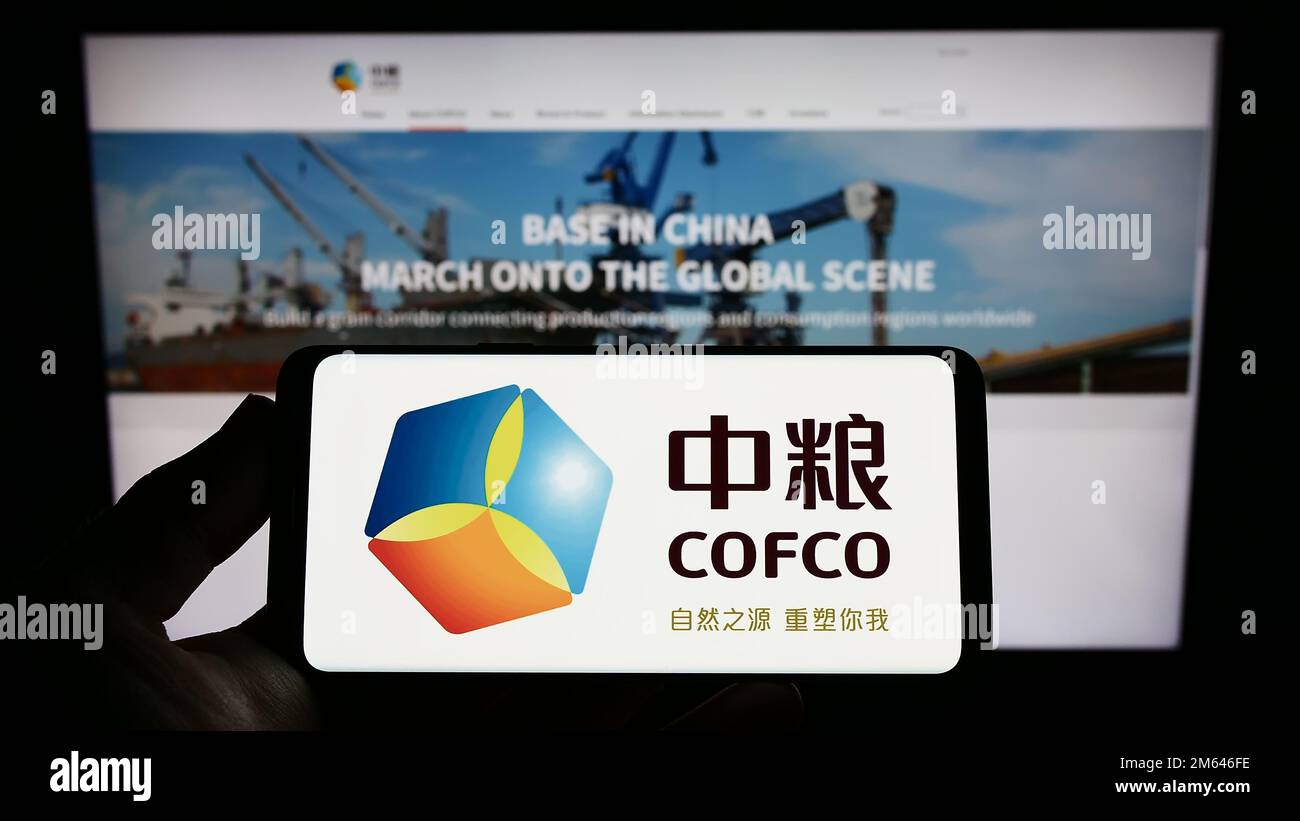 Persona che tiene in mano uno smartphone con il logo di China Oil and Food Corporation (COFCO) sullo schermo davanti al sito Web. Messa a fuoco sul display del telefono. Foto Stock