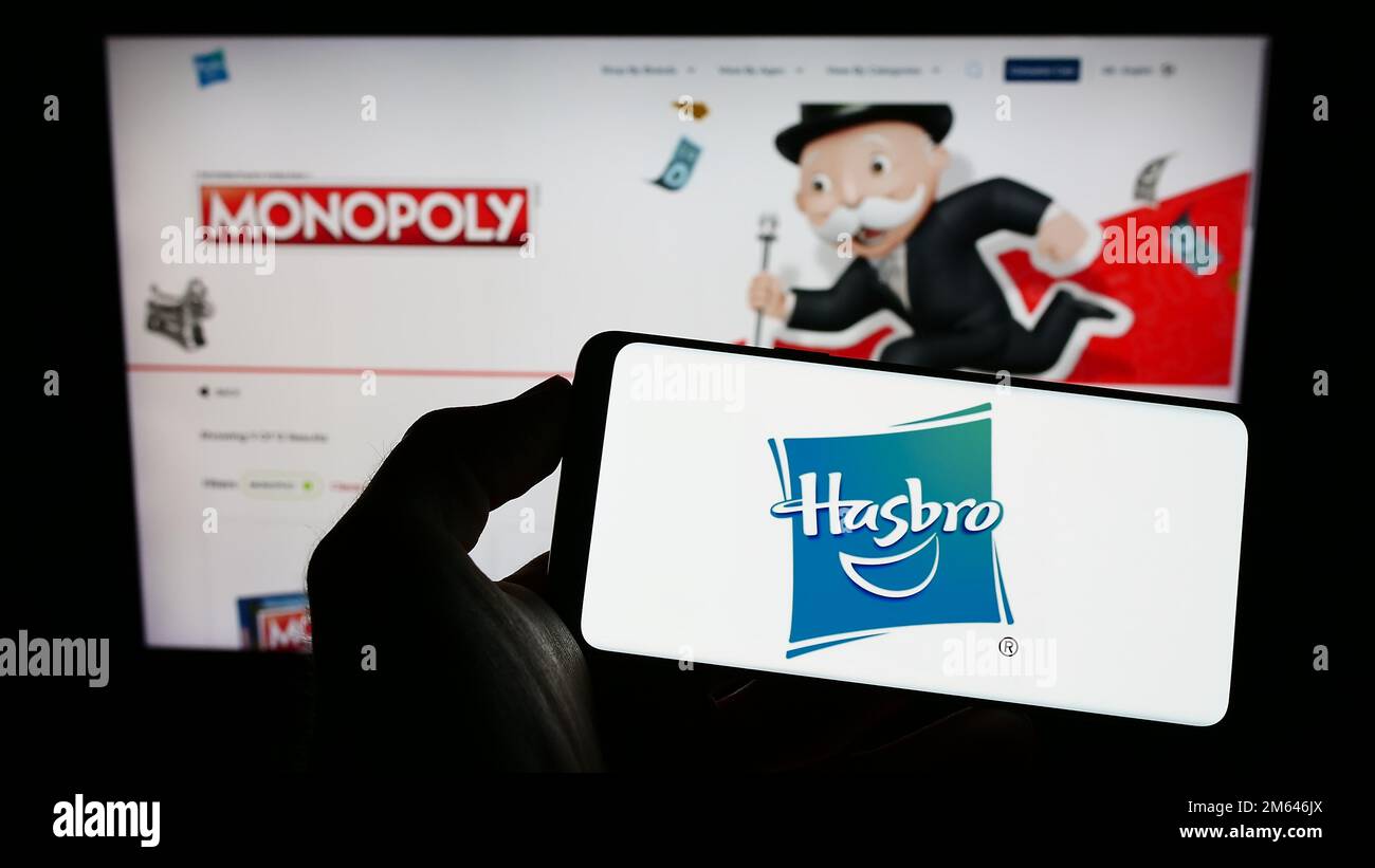 Persona che tiene il cellulare con il logo della società americana di giocattoli e intrattenimento Hasbro Inc. Sullo schermo di fronte alla pagina web. Messa a fuoco sul display del telefono. Foto Stock