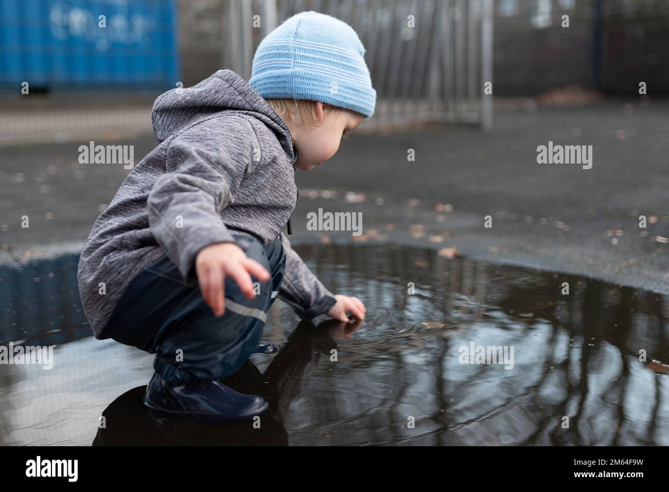 ragazzo di due anni con pantaloni e stivali da pioggia che gioca in una pozza d'acqua dopo la doccia a pioggia Foto Stock