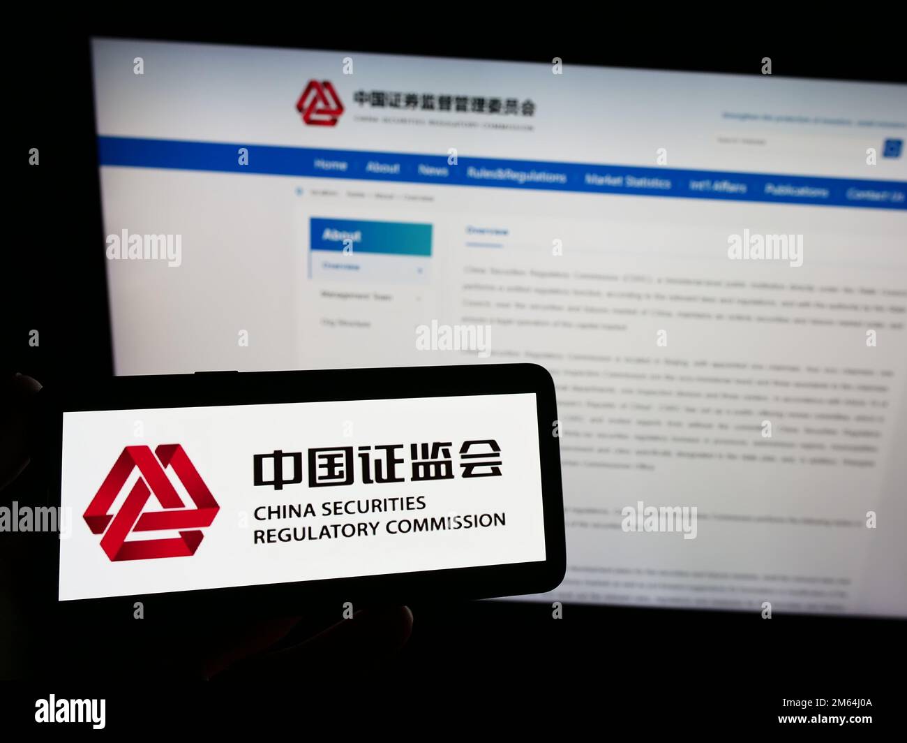 Persona che tiene in mano uno smartphone con il logo della China Securities Regulatory Commission (CSRC) sullo schermo di fronte al sito Web. Messa a fuoco sul display del telefono. Foto Stock