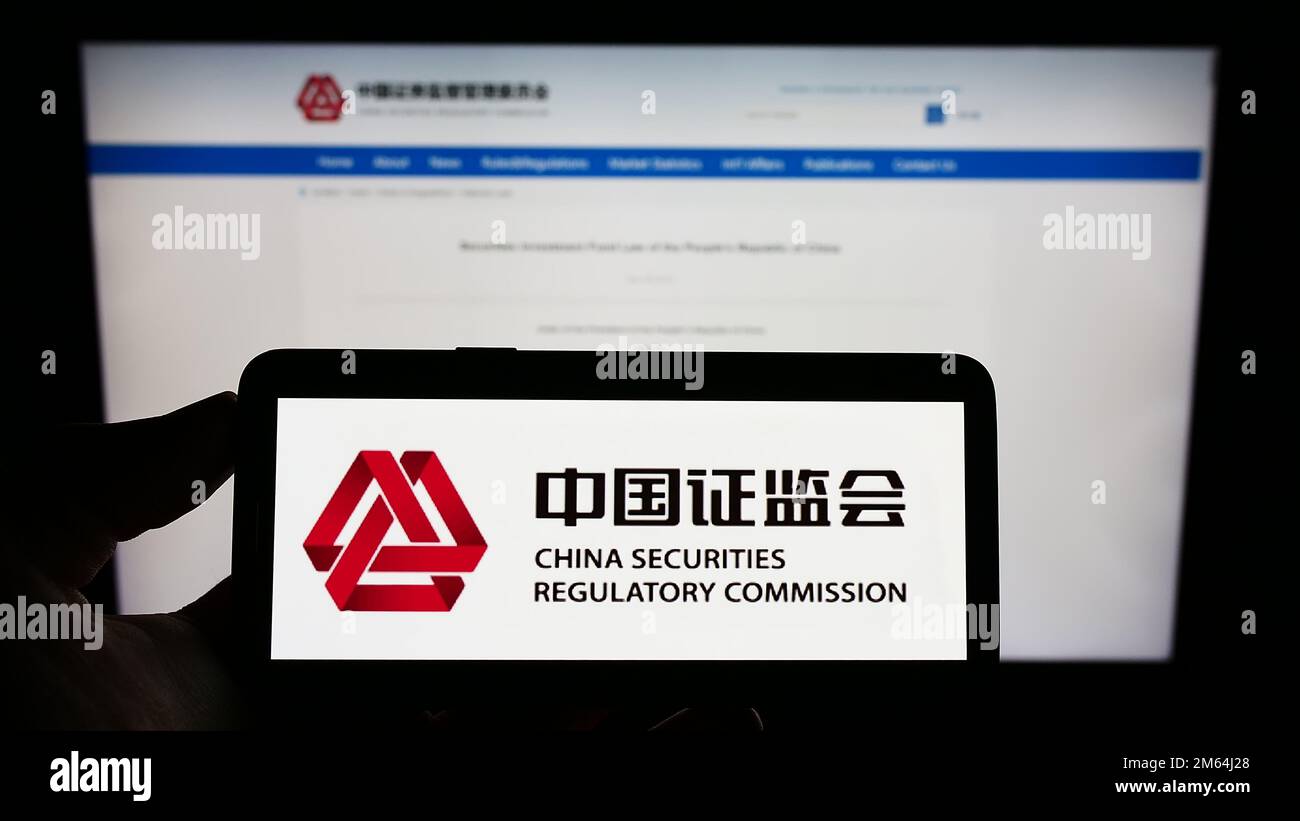 Persona che tiene il cellulare con il logo della China Securities Regulatory Commission (CSRC) sullo schermo di fronte alla pagina Web. Messa a fuoco sul display del telefono. Foto Stock