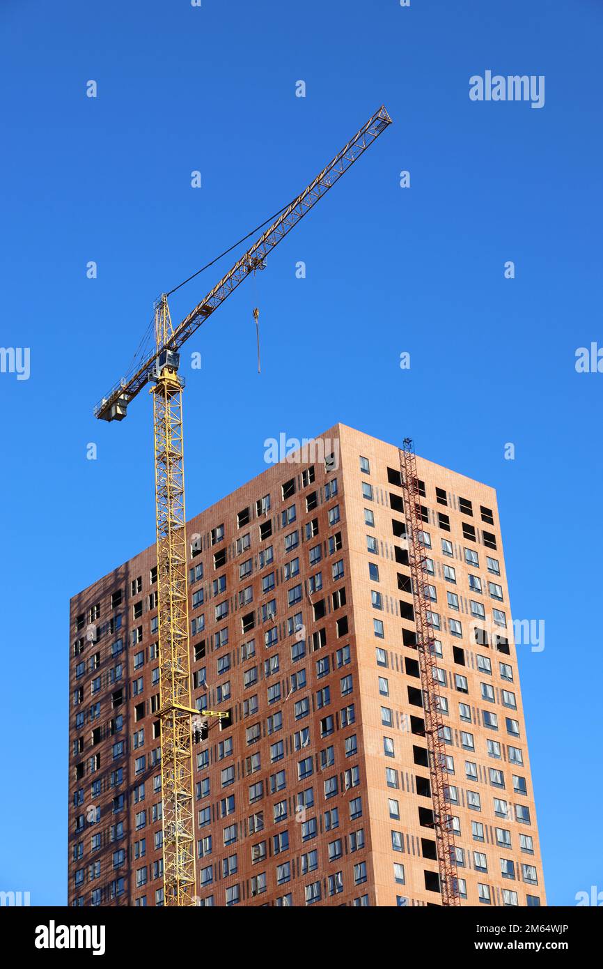 Gru a torre e edificio incompiuto sullo sfondo del cielo blu, tiro verticale. Edilizia abitativa, condomini in città Foto Stock