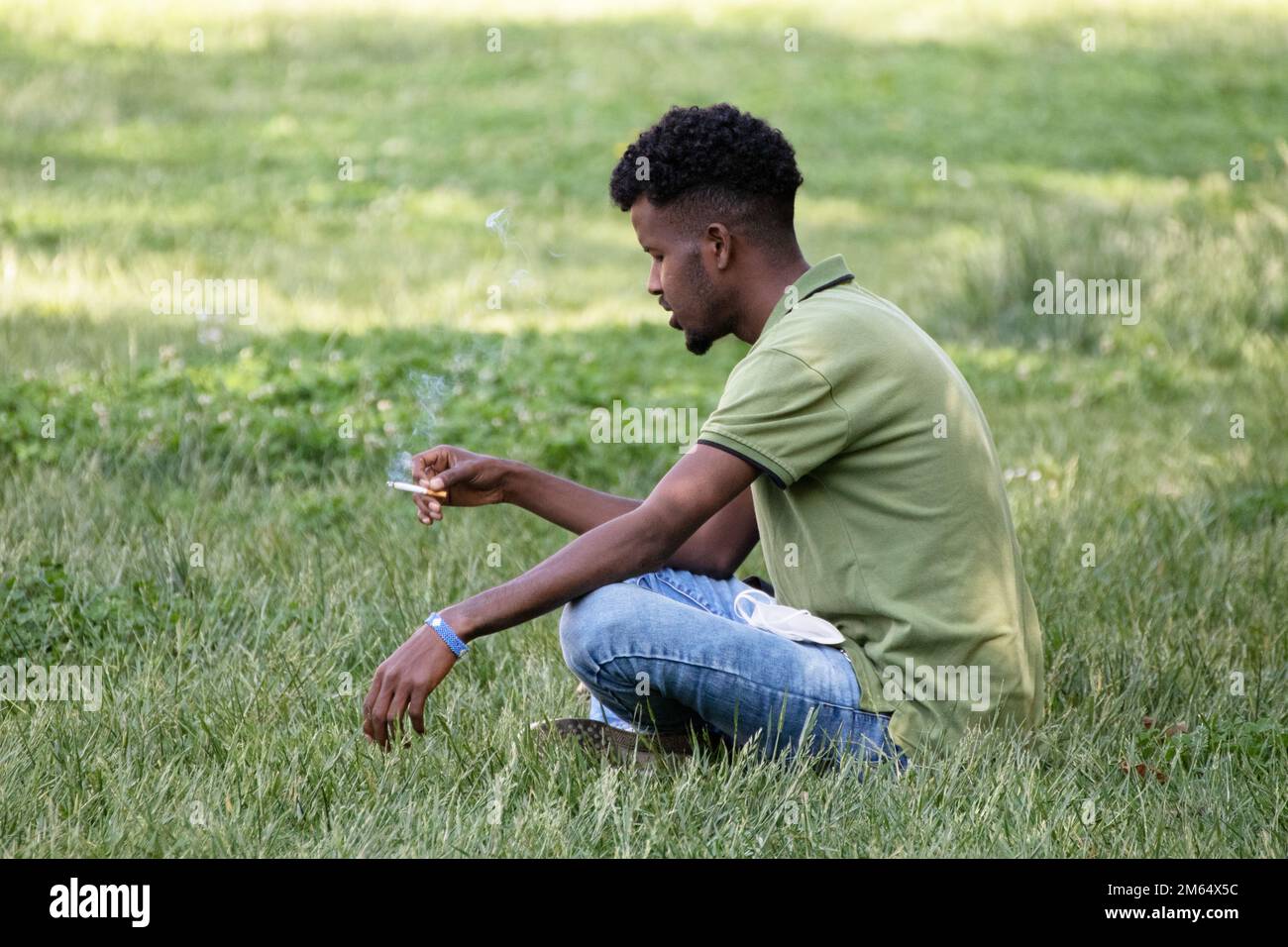 il giovane fuma seduto sull'erba nel parco cittadino Foto Stock