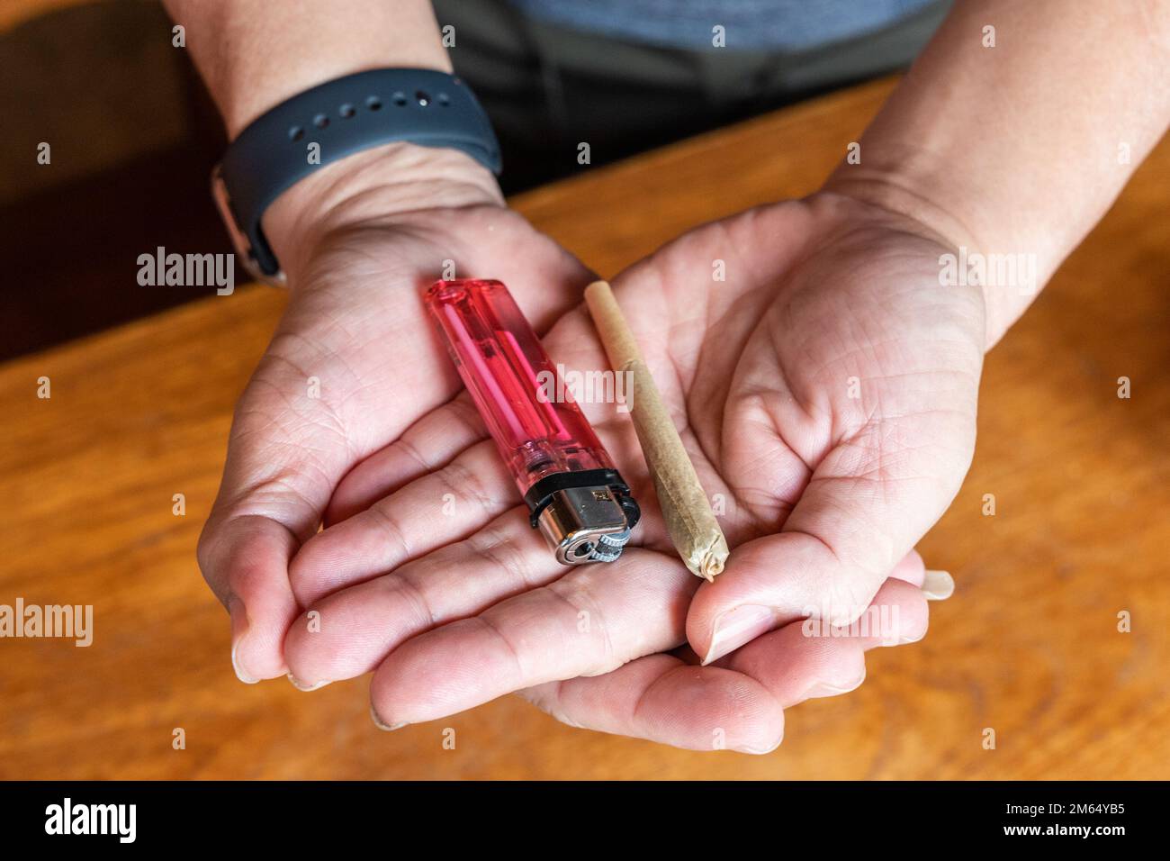 La sigaretta di cannabis e l'accendisigari a mano sono pronti per essere fumati Foto Stock