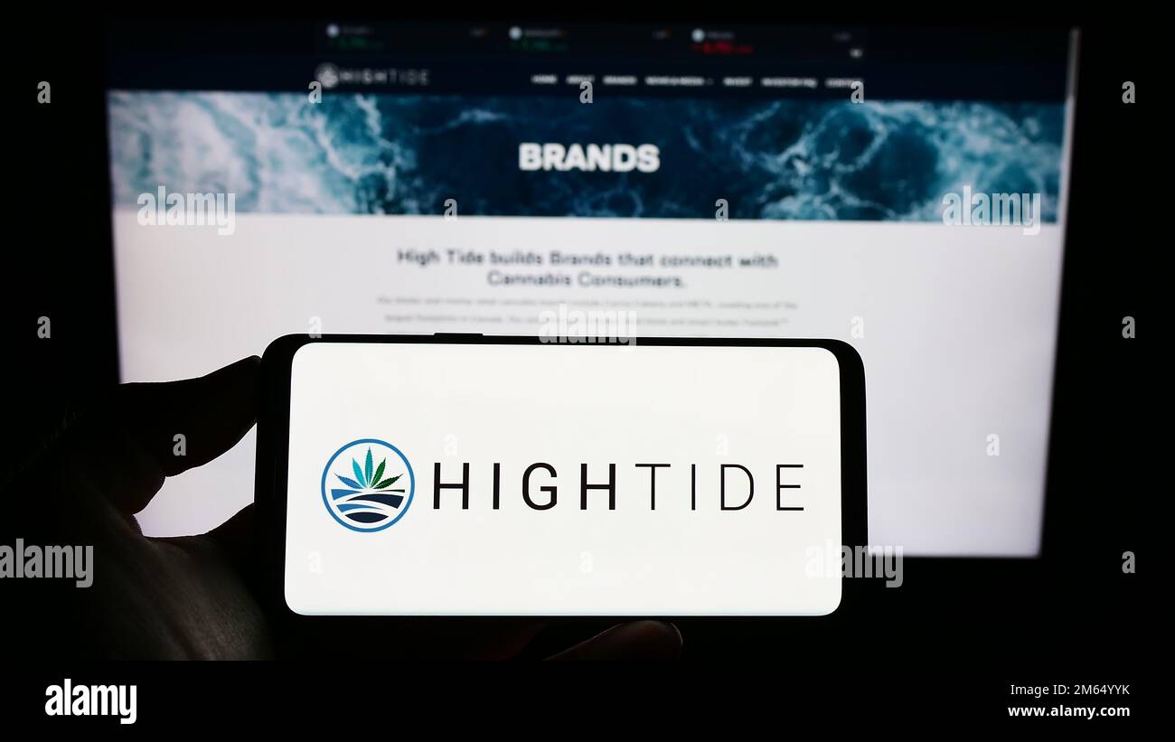 Persona che tiene un telefono cellulare con il logo della società canadese di cannabis High Tide Inc. Sullo schermo di fronte alla pagina web aziendale. Messa a fuoco sul display del telefono. Foto Stock