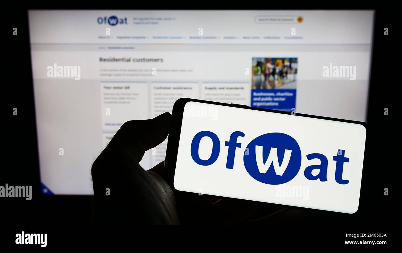 Persona che tiene il cellulare con il logo dell'autorità di regolamentazione dei servizi idrici (Ofwat) sullo schermo di fronte alla pagina web. Messa a fuoco sul display del telefono. Foto Stock