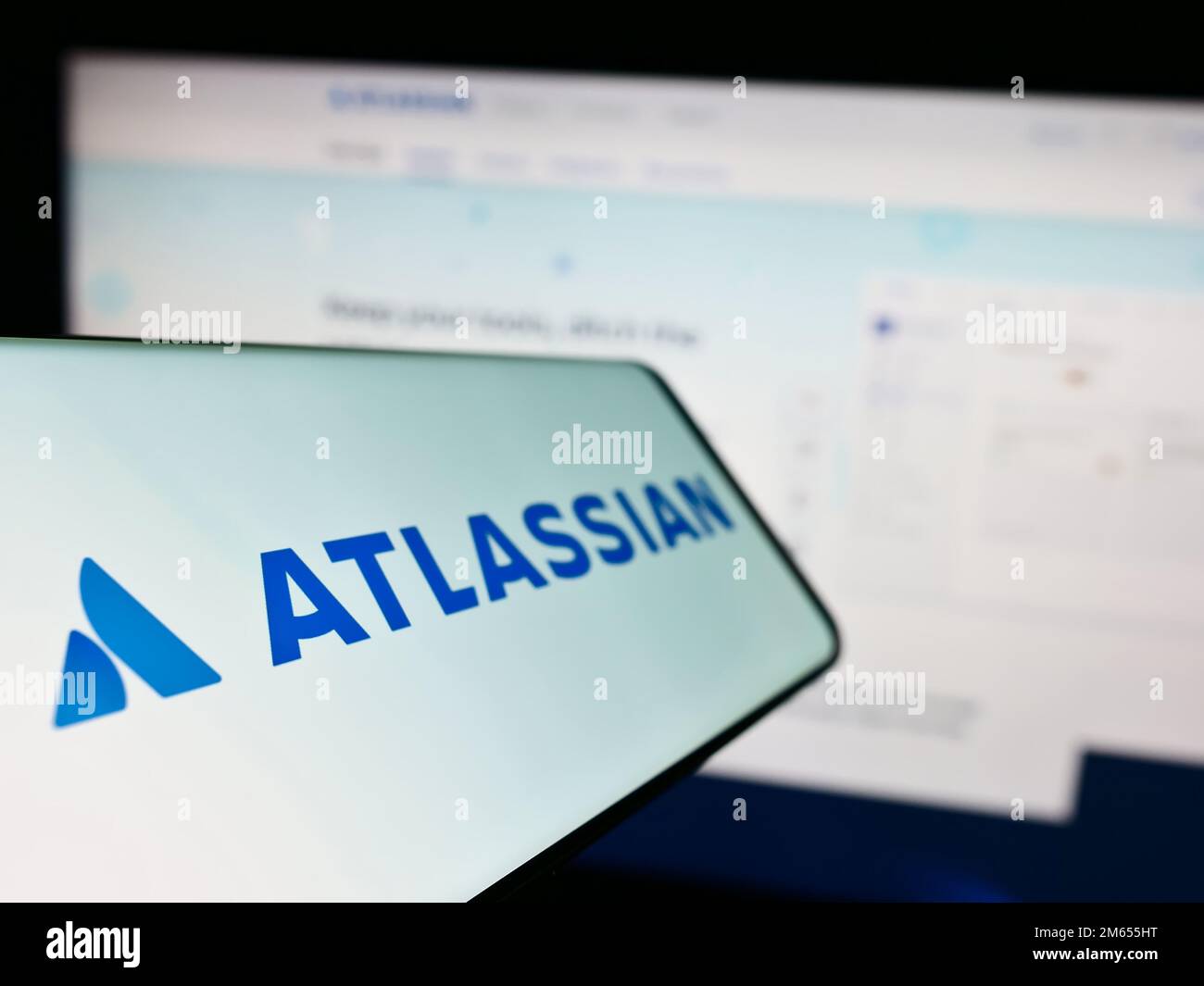 Cellulare con il logo della società australiana di software Atlassian Corporation sullo schermo di fronte al sito web aziendale. Messa a fuoco a sinistra del display del telefono. Foto Stock