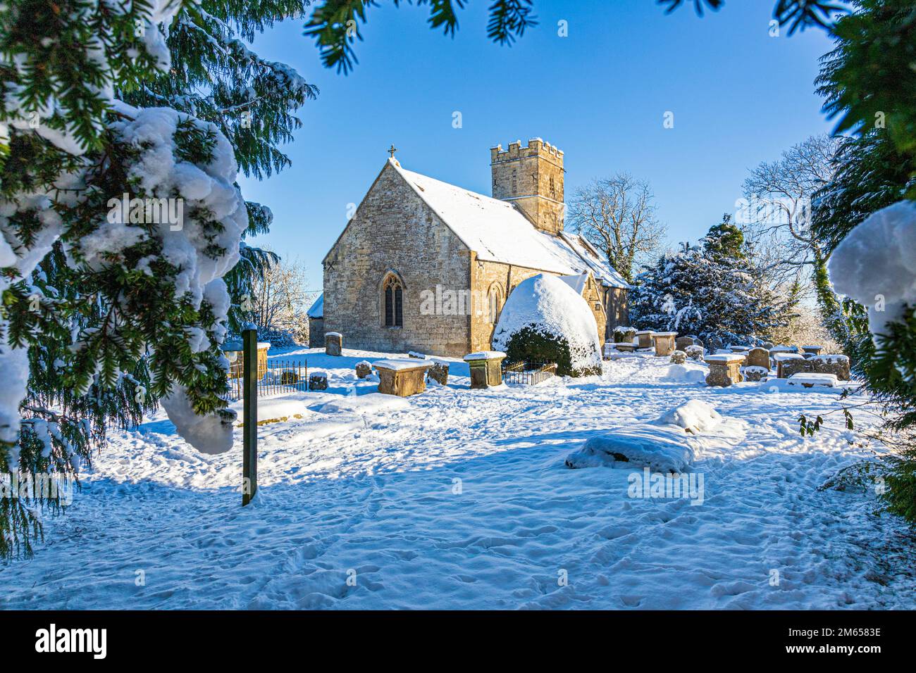 Neve d'inverno all'inizio della chiesa di St Michael & All Angels del 12th ° secolo nel villaggio di Cotswold di Bridpsfield, Gloucestershire, Inghilterra UK Foto Stock