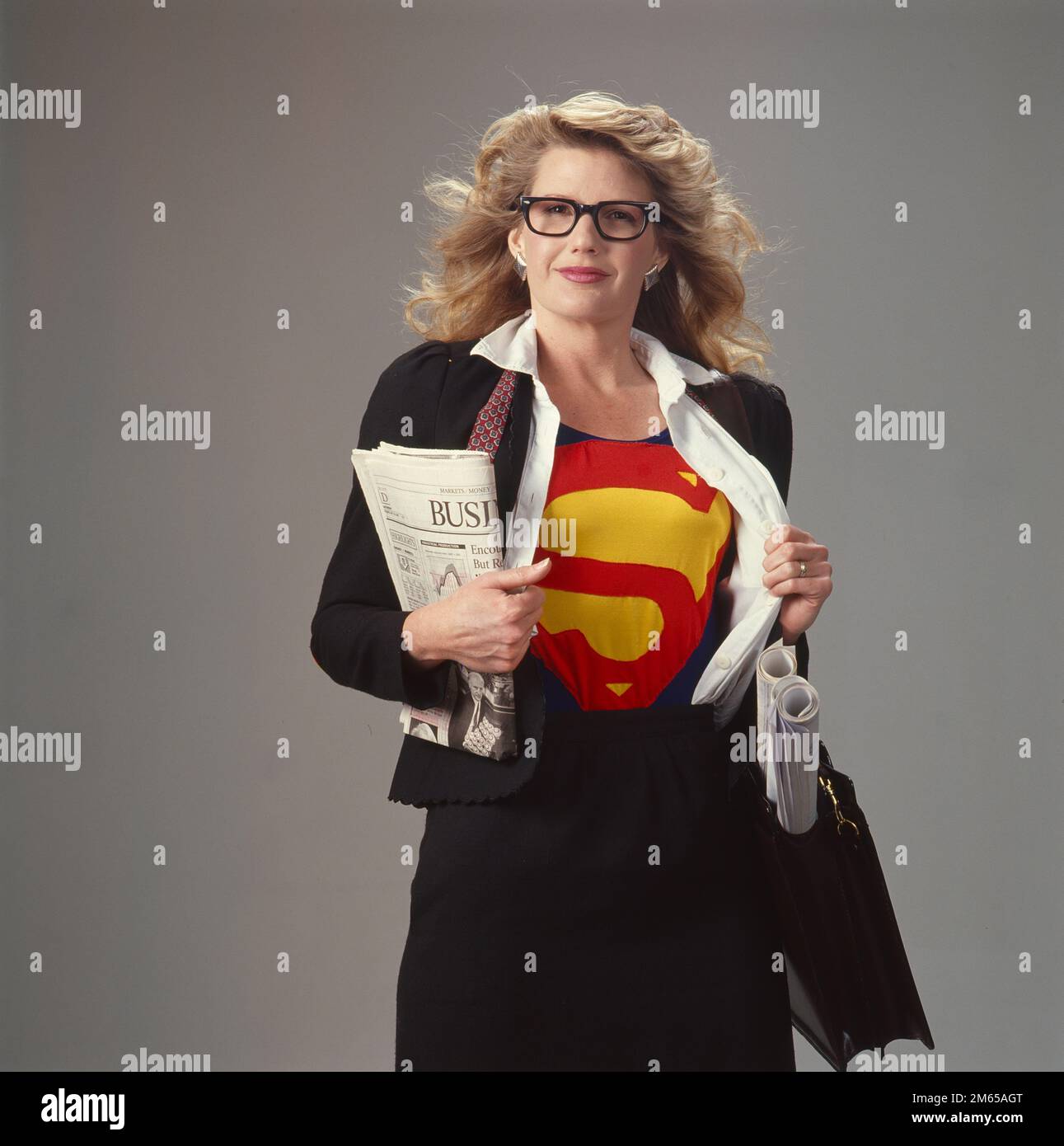 Supermom giovane donna di affari che indossa il logo Superman sulla sua camicia mentre in abbigliamento di affari che tiene un giornale e il trasporto BluePrint Foto Stock