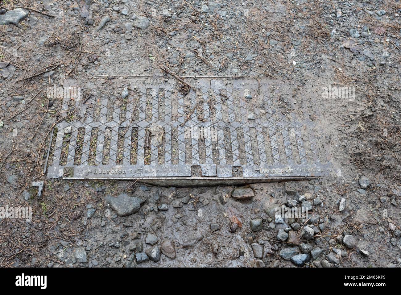 Canale di drenaggio o canale di drenaggio bloccato con terreno e ghiaia che non possono essere utilizzati per dirigere l'acqua piovana dalla strada a causa della mancanza di manutenzione Foto Stock