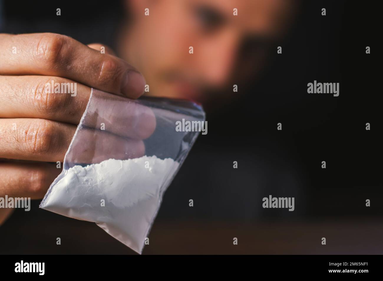 Concetto di tossicodipendenza. La mano dell'uomo tiene il pacchetto o il sacchetto di plastica con la cocaina o altre droghe, l'abuso della droga e il concetto di dipendenza di pericolo. Foto Stock