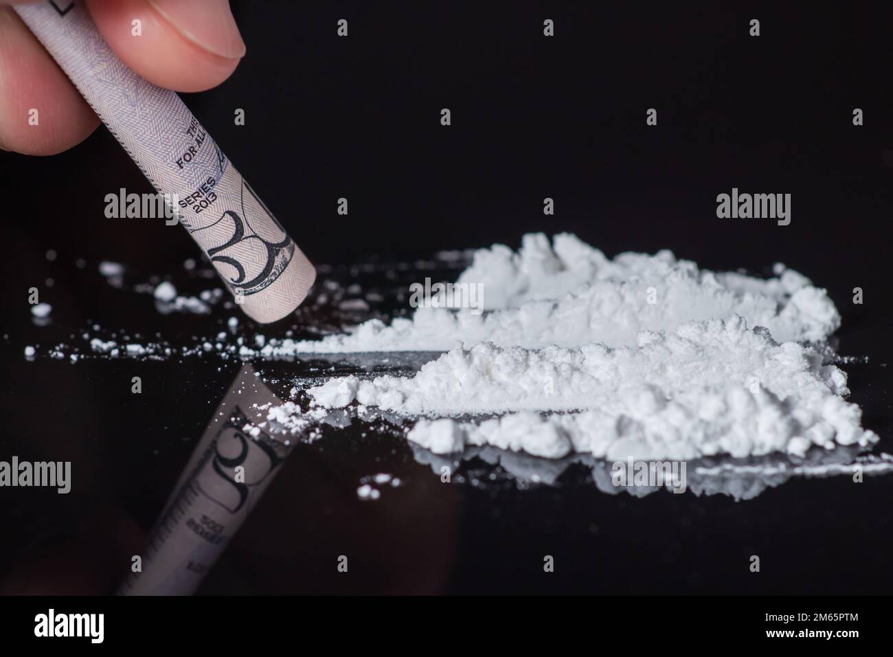 Le mani dell'uomo rotola la banconota per usare le linee della polvere della cocaina. Concetto di tossicodipendenza. Una linea di coke su sfondo nero. Concetto di dipendenza. Mefedrone, Foto Stock