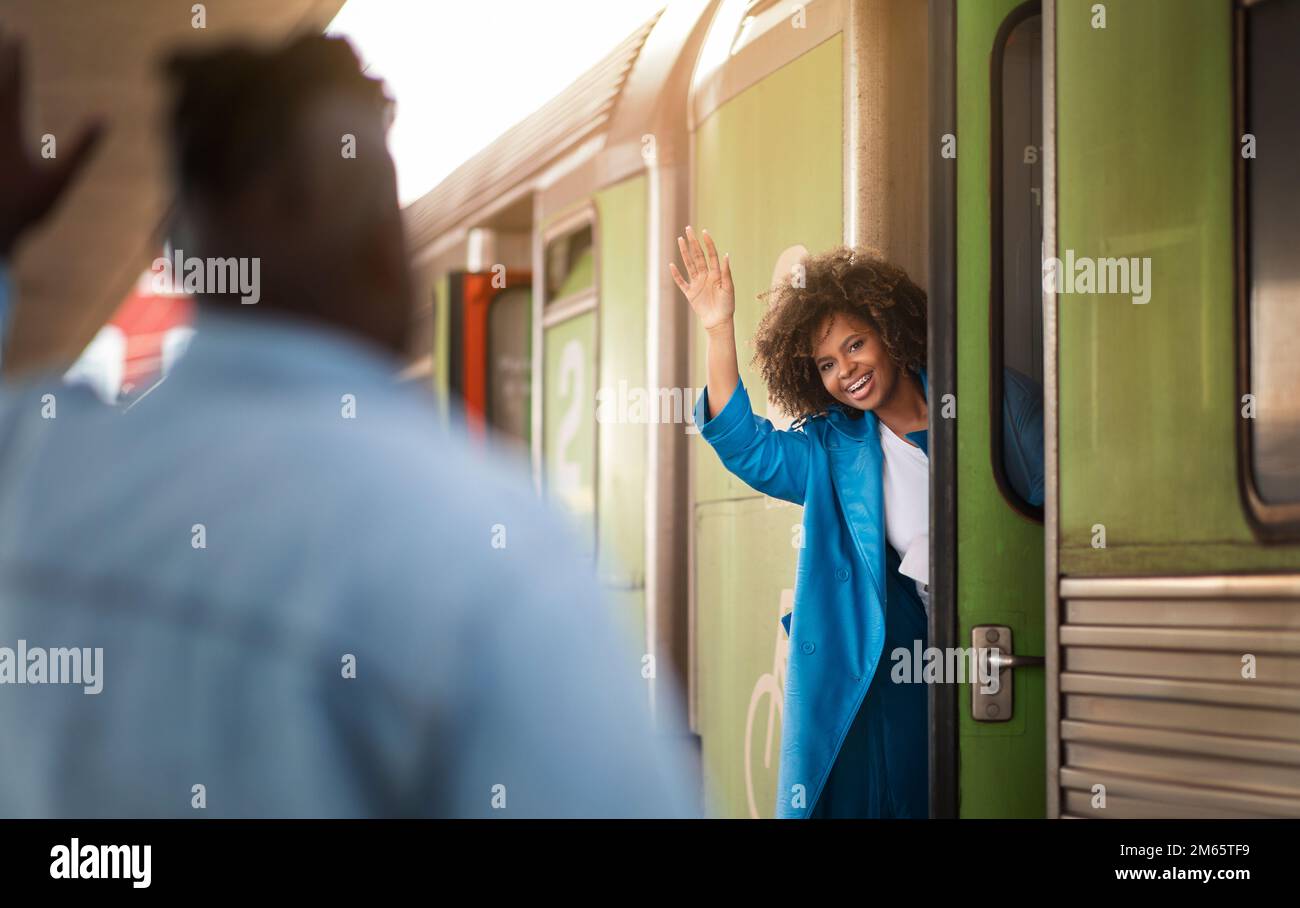Donna nera felice che agita la mano al ragazzo mentre si trova in piedi in Train Door Foto Stock