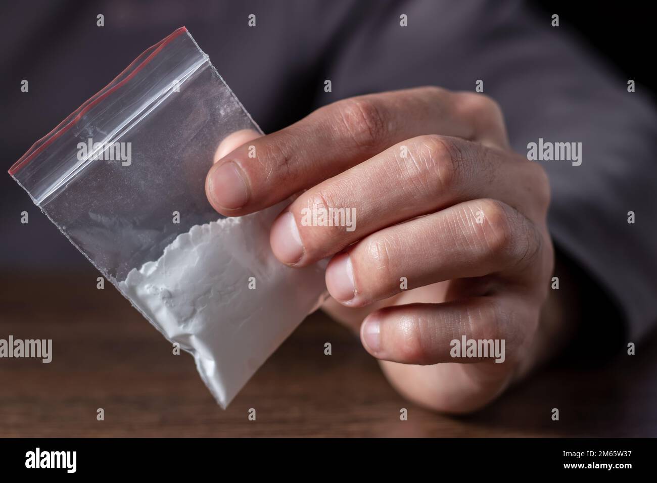 Concetto di tossicodipendenza. La mano dell'uomo tiene il pacchetto o il sacchetto di plastica con la cocaina o altre droghe, l'abuso della droga e il concetto di dipendenza di pericolo. Foto Stock