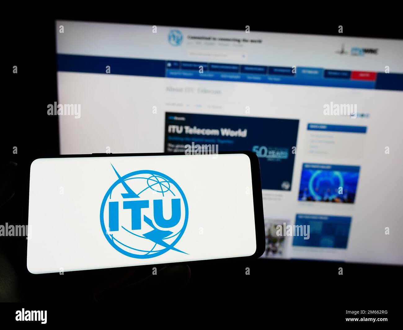 Persona che tiene in mano uno smartphone con il logo dell'Unione internazionale delle telecomunicazioni (ITU) sullo schermo di fronte al sito Web. Messa a fuoco sul display del telefono. Foto Stock