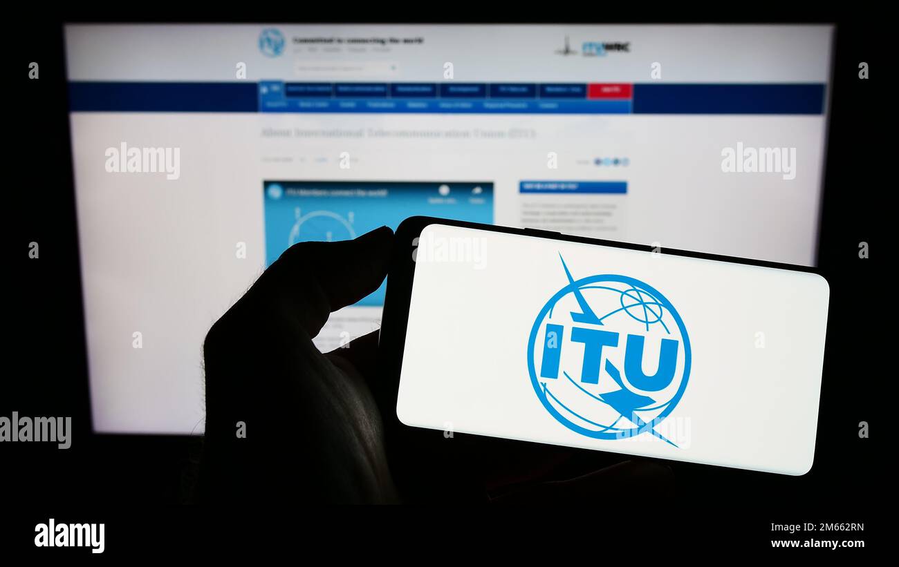 Persona che tiene un telefono cellulare con il logo dell'Unione internazionale delle telecomunicazioni (ITU) sullo schermo davanti alla pagina web. Messa a fuoco sul display del telefono. Foto Stock