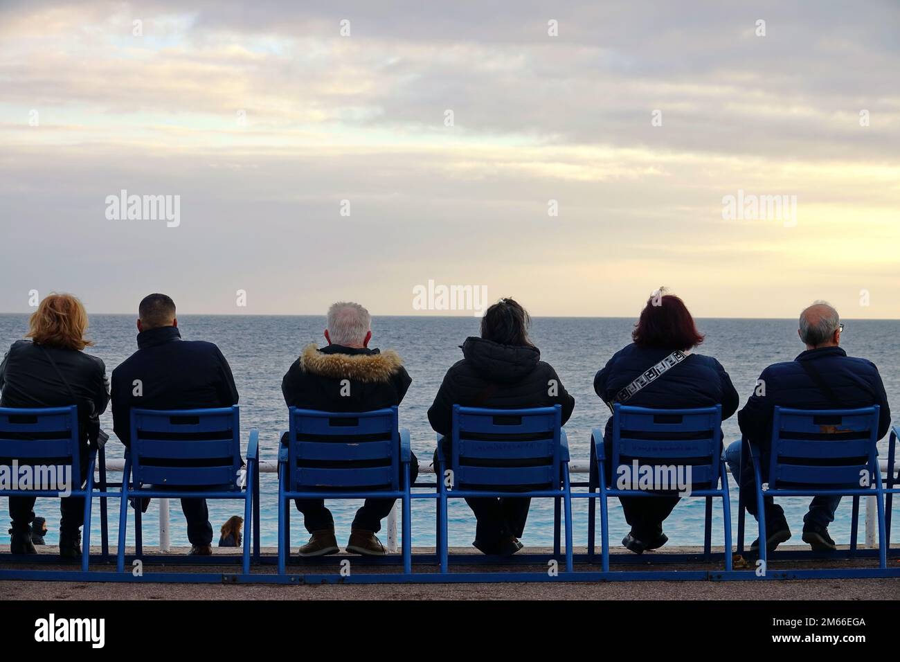 Persone sedute davanti al mare sulle famose sedie blu di Nizza, sulla Promenade des Anglais. Nizza, Francia - Dicembre 2022 Foto Stock