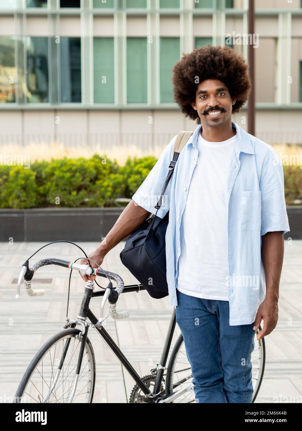 Giovane afro-americano sorridente con capelli afro in una città con una bicicletta che guarda la macchina fotografica Foto Stock