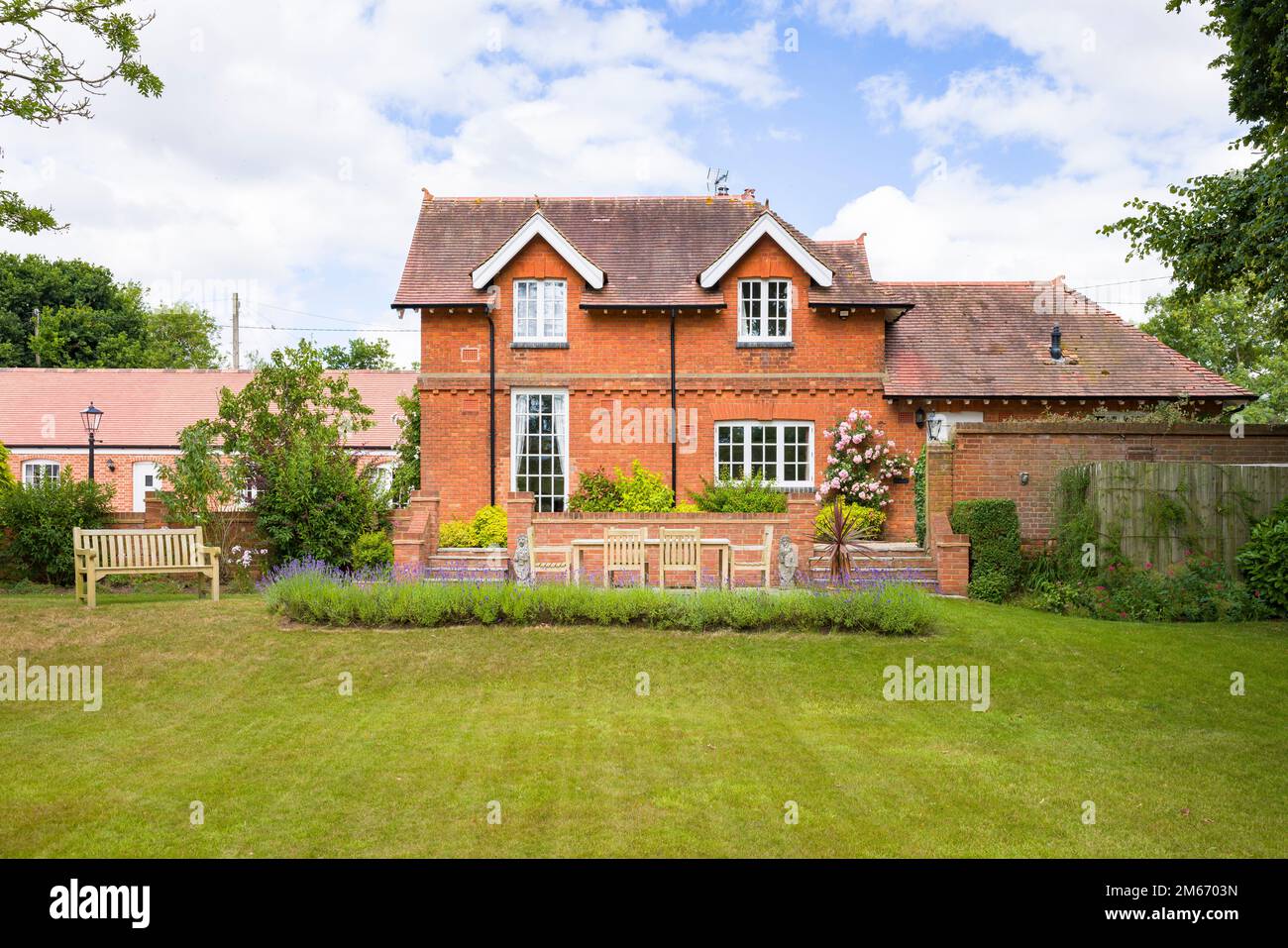 Grande casa di campagna inglese e giardino in estate con prato e terrazza patio con mobili da giardino in teak Foto Stock