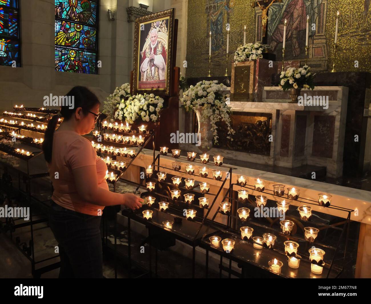 Manila, Filippine. 02nd Jan, 2023. Una donna accende una candela in onore del compianto Pontefice, il compianto Papa emerito Benedetto XVI. I devoti cattolici rendono il loro ultimo rispetto a Papa Emerito Benedetto XVI offrendo preghiere, illuminando candele e scrivendo il libro delle condoglianze per il pontefice tardivo nella Cappella di Cristo Re della Cattedrale di Manila lunedì 2 gennaio. Il defunto papa, il cui nome di nascita era Joseph Aloisius Ratzinger, morì all'età di 95 anni il 31 dicembre 2022 presso il Monastero Mater Ecclesiae nella Città del Vaticano. Credit: SOPA Images Limited/Alamy Live News Foto Stock