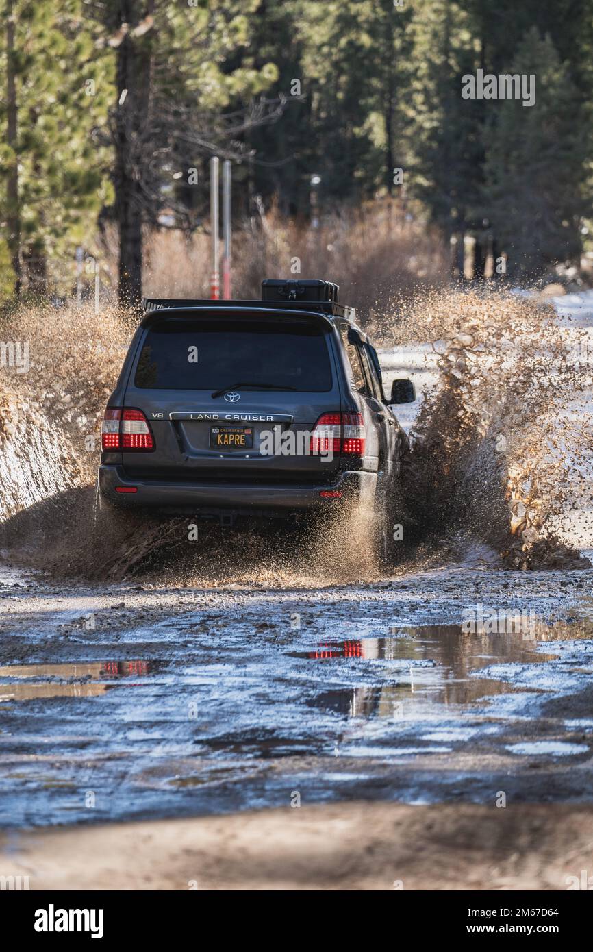 Vista dall'angolo posteriore del SUV fuoristrada Overland Land Cruiser che attraversa l'acqua su un sentiero innevato nella foresta Foto Stock
