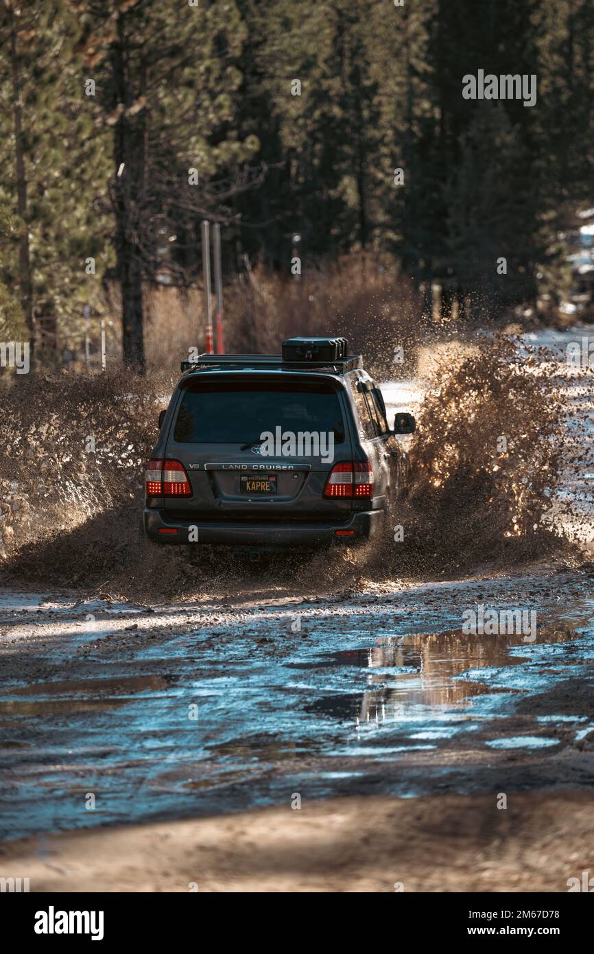 Vista dall'angolo posteriore del SUV fuoristrada Overland Land Cruiser che attraversa l'acqua su un sentiero innevato nella foresta Foto Stock