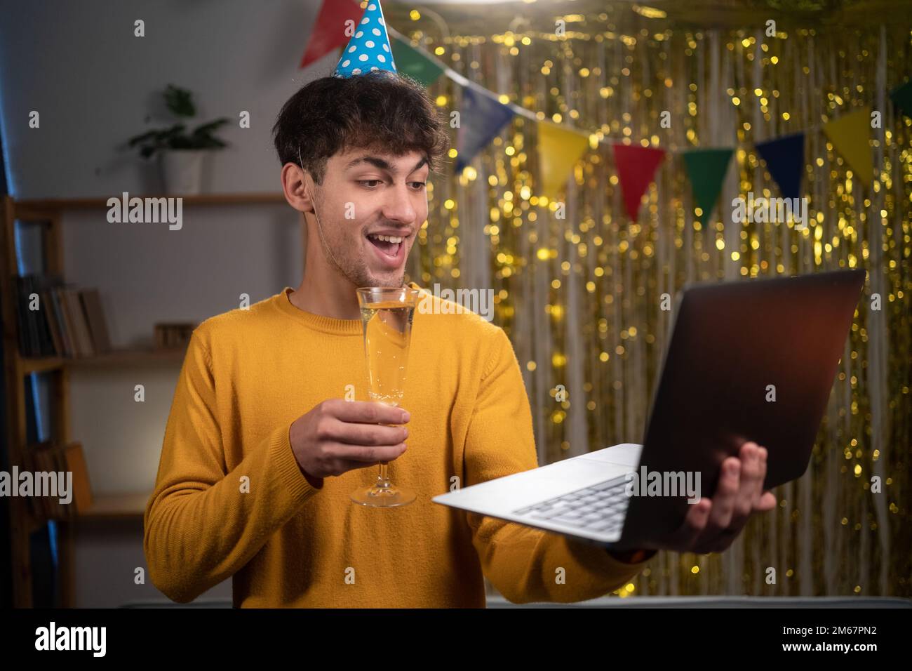 Giovane arabo che festeggia il suo compleanno con una videochiamata con gli amici usando un computer portatile. Bicchiere con champagne. Autentico Foto Stock