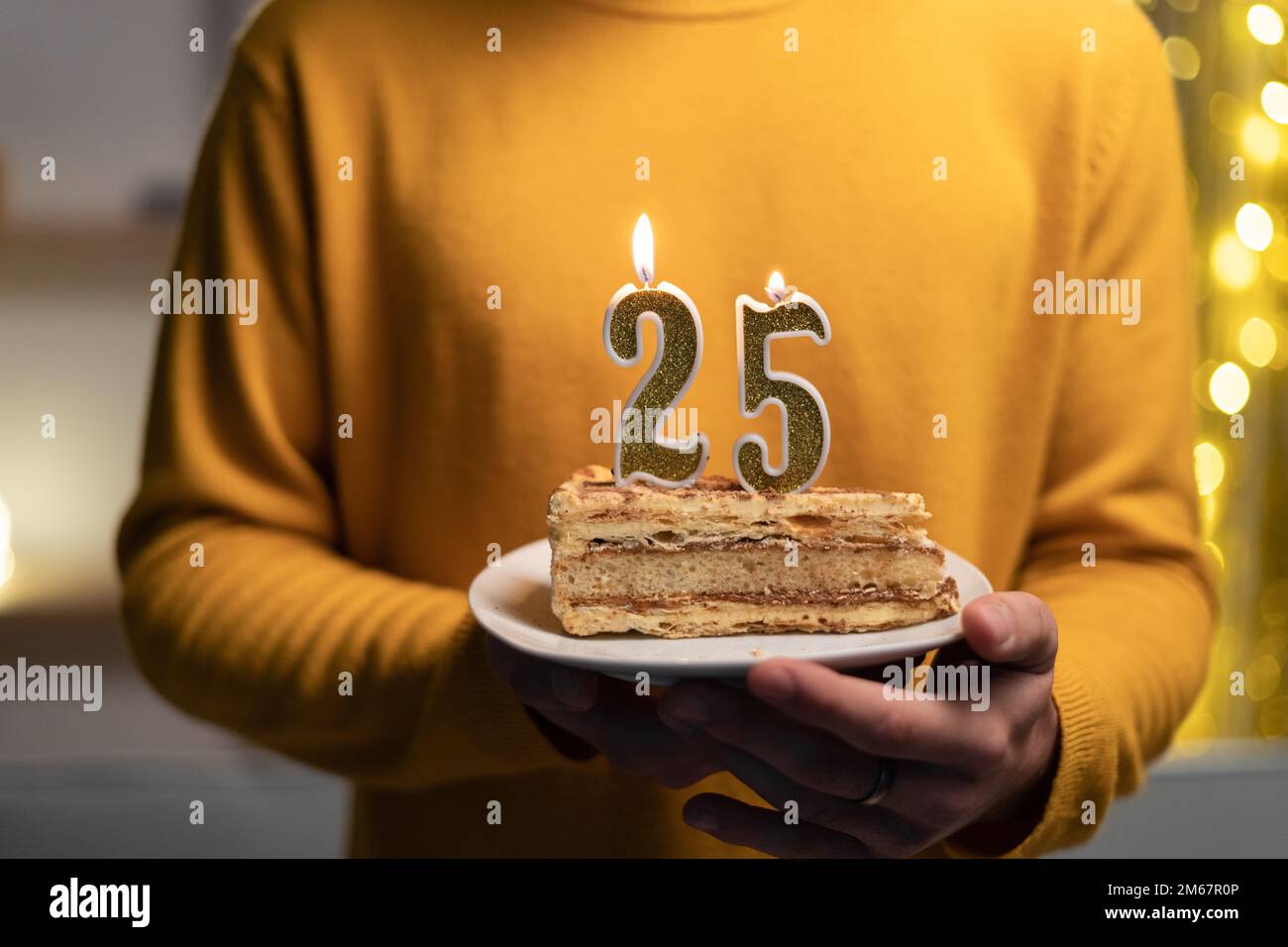 Torta con il numero 25 candele accese in mani maschili. 25th compleanno Foto Stock