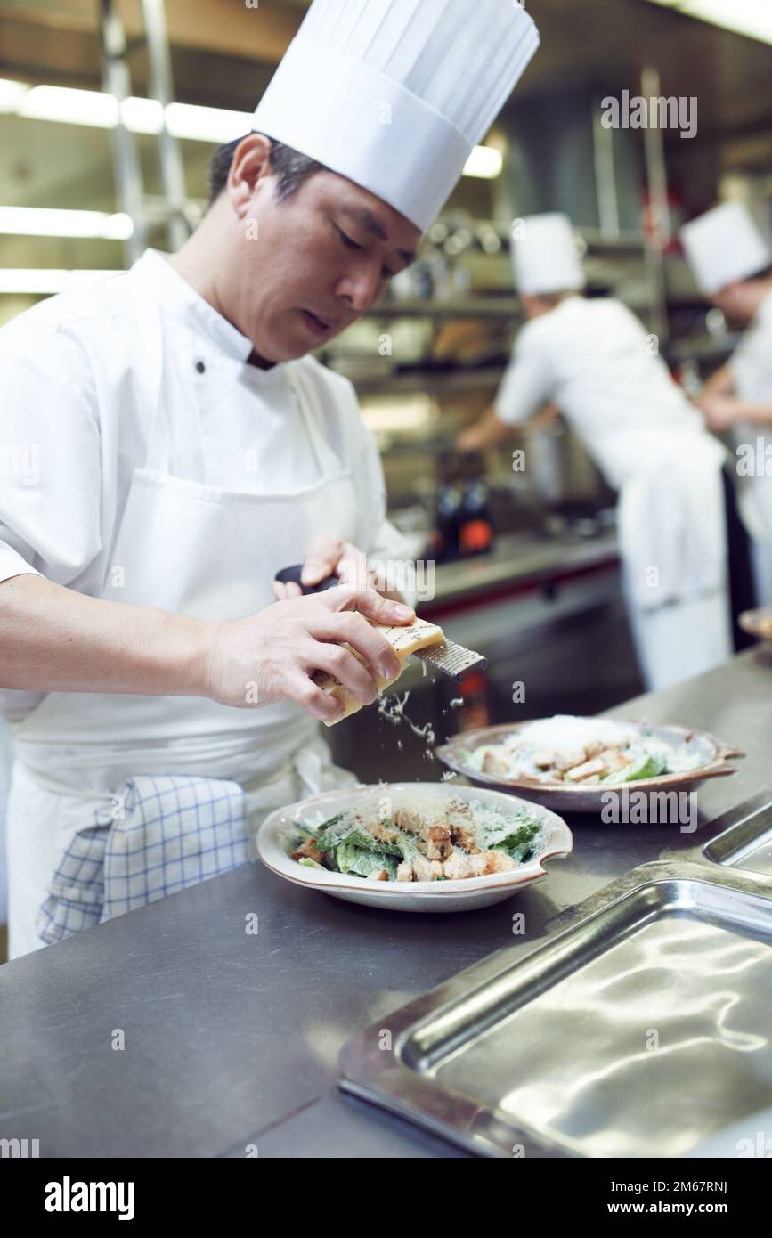 Tutto meglio con il parmigiano. chef che preparano un servizio di pasto in una cucina professionale. Foto Stock