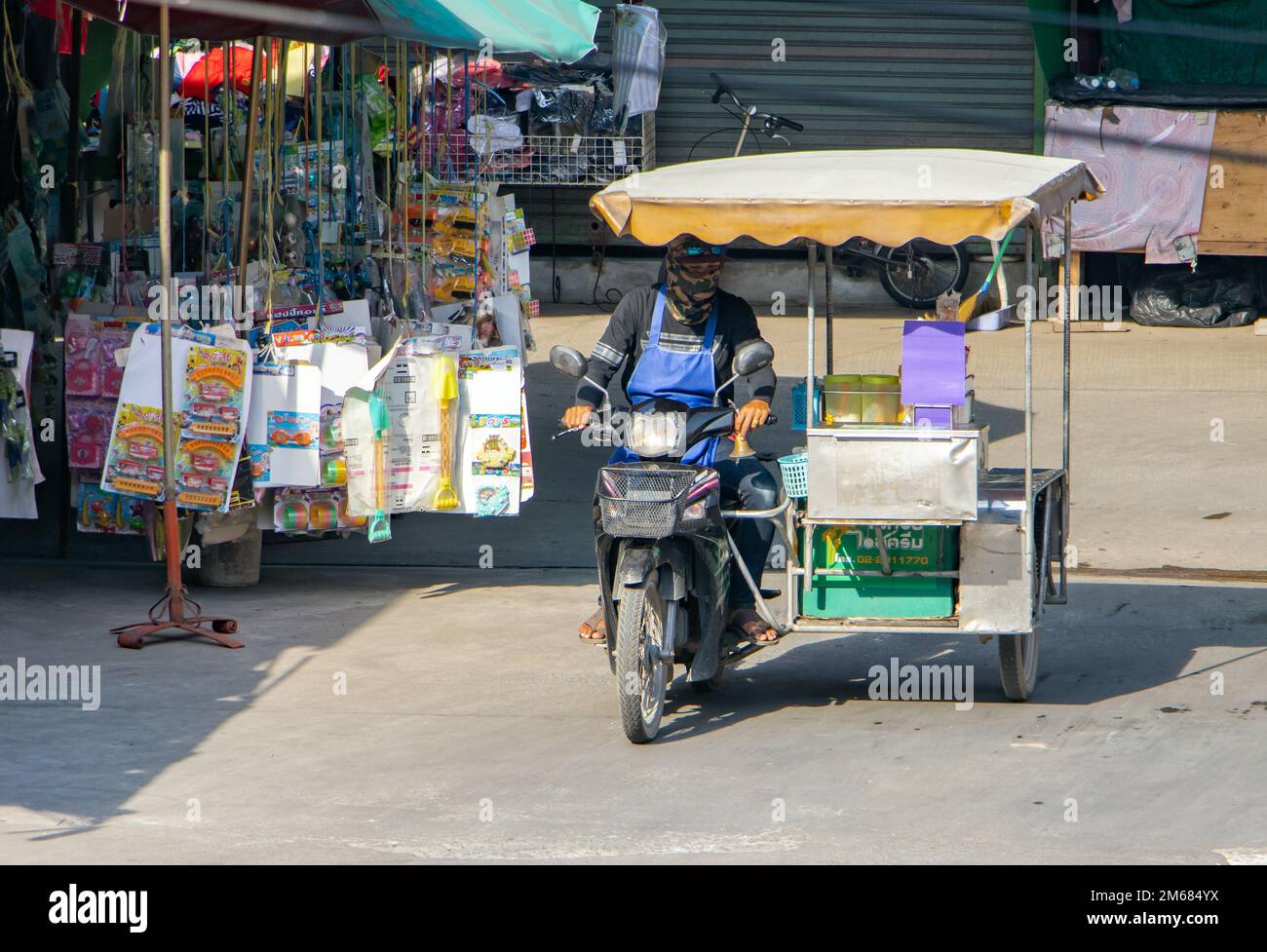 SAMUT PRAKAN, THAILANDIA, ottobre 19 2022, un distributore di gelati guida una moto a tre ruote lungo una strada cittadina Foto Stock