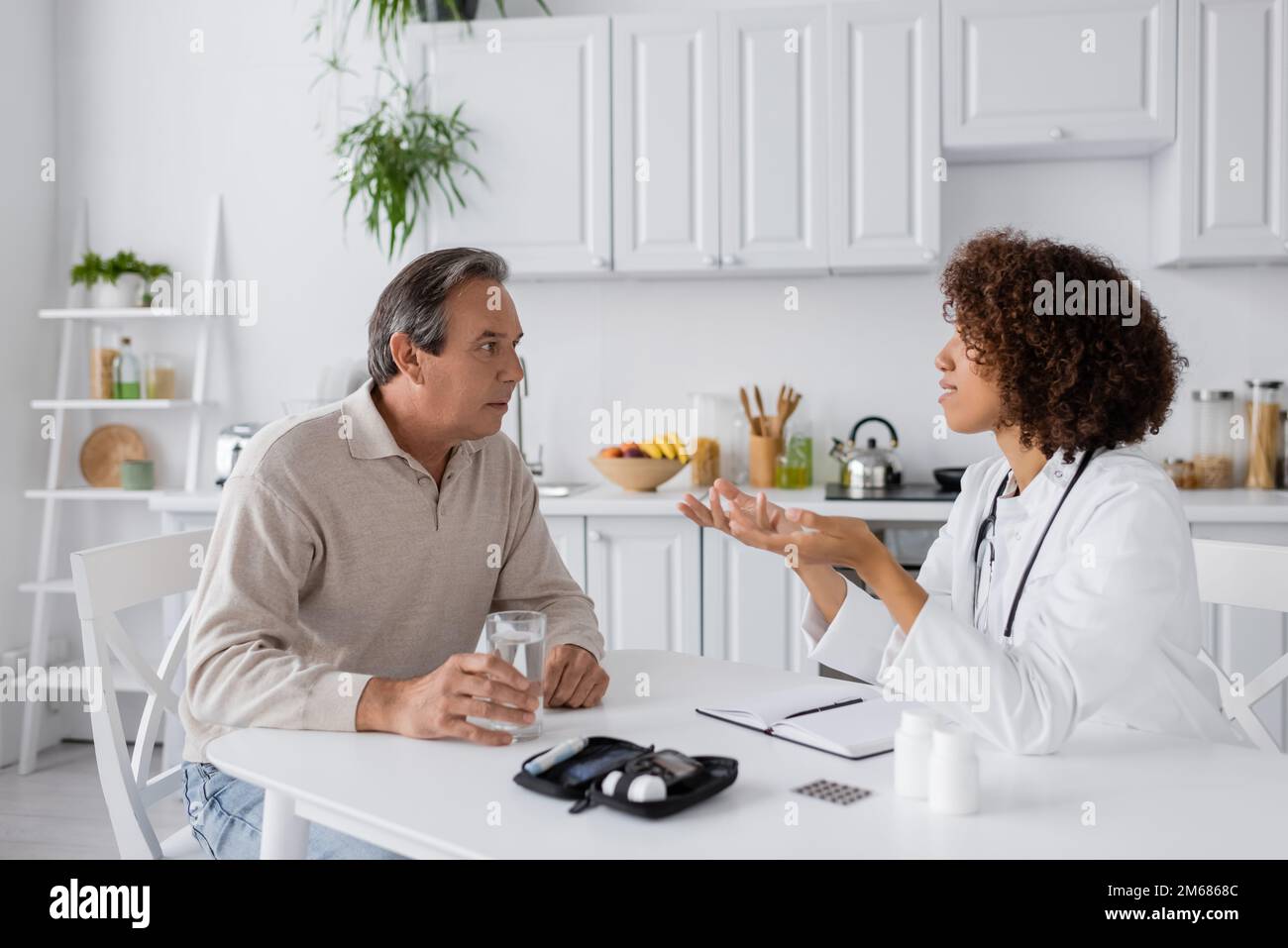 curly afroamericano medico gesturing mentre si parla con paziente di mezza età vicino al glucometro dispositivo, immagine stock Foto Stock