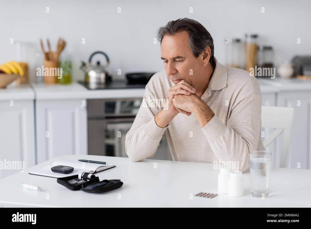 uomo pensivo e di mezza età con diabete guardando glucometro e penna lancetta sul tavolo, immagine stock Foto Stock