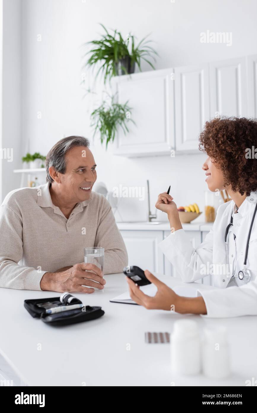 curly medico afroamericano che tiene glucometro vicino sorridente paziente di mezza età, immagine di scorta Foto Stock