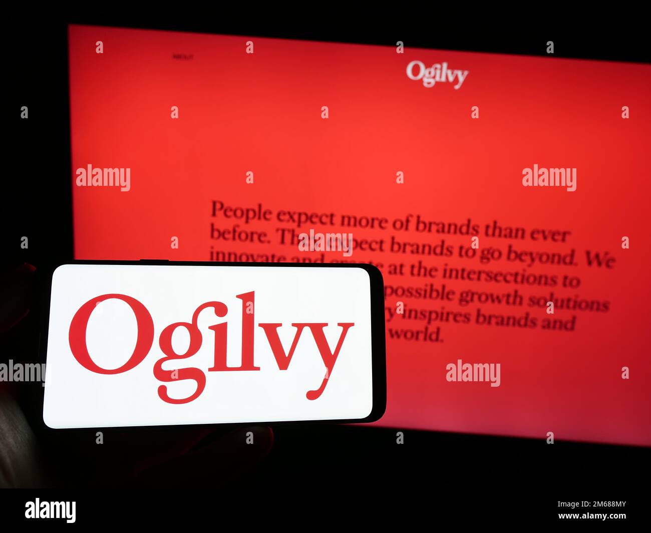 Persona che tiene lo smartphone con il logo della società di pubblicità Ogilvy sullo schermo di fronte al sito Web. Messa a fuoco sul display del telefono. Foto Stock
