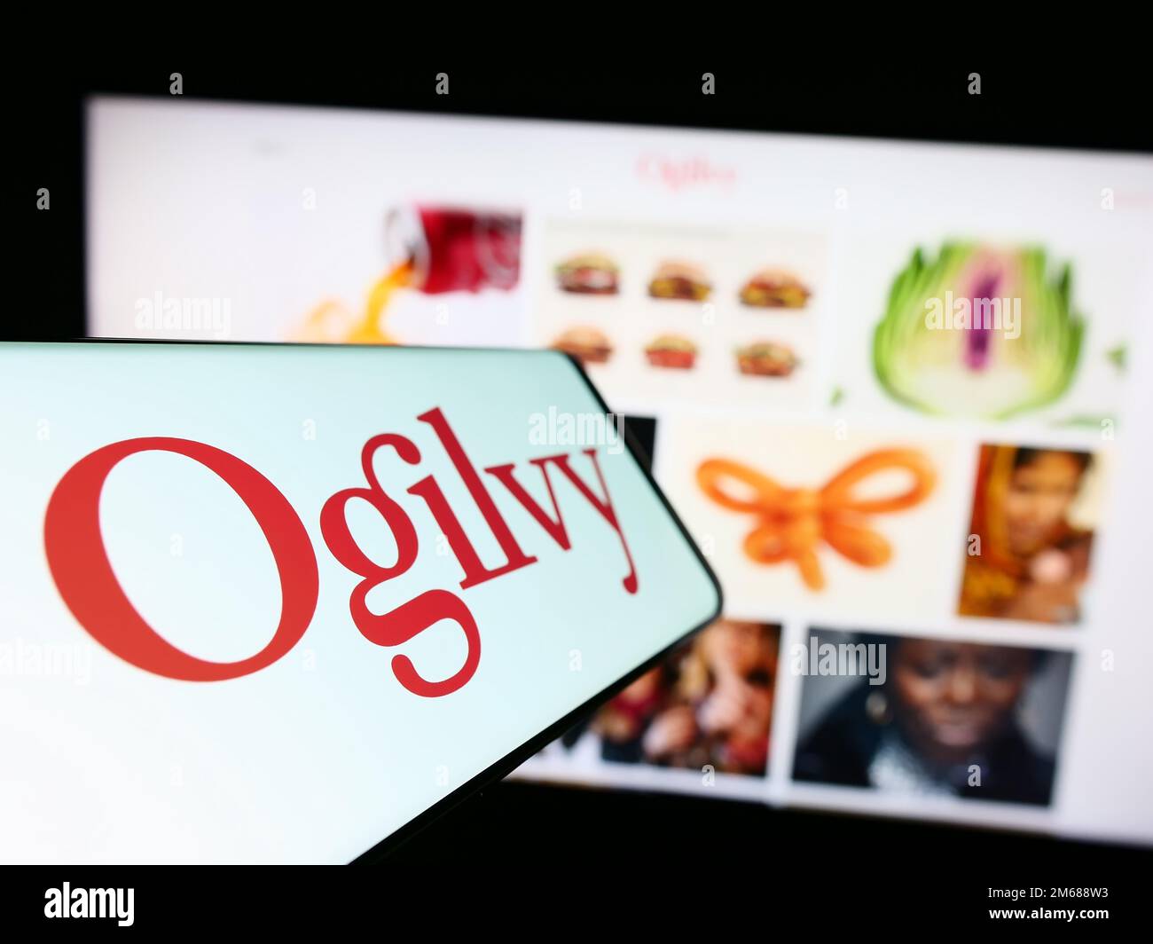 Smartphone con il logo della società di pubblicità Ogilvy sullo schermo di fronte al sito Web aziendale. Messa a fuoco al centro a sinistra del display del telefono. Foto Stock