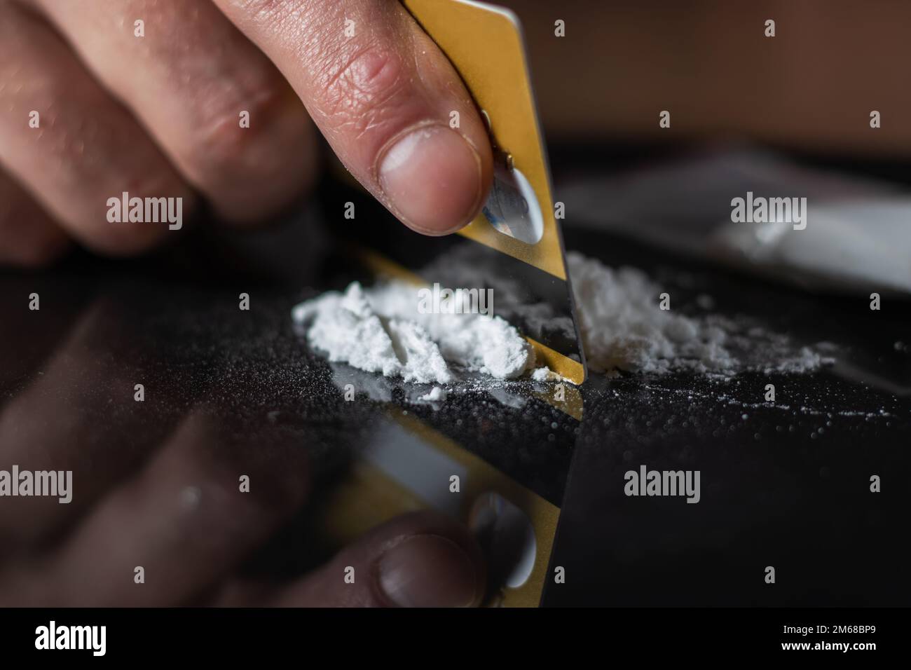 L'uomo usa la carta di credito per fare le linee della polvere della droga della cocaina sul tavolo nero. Foto Stock