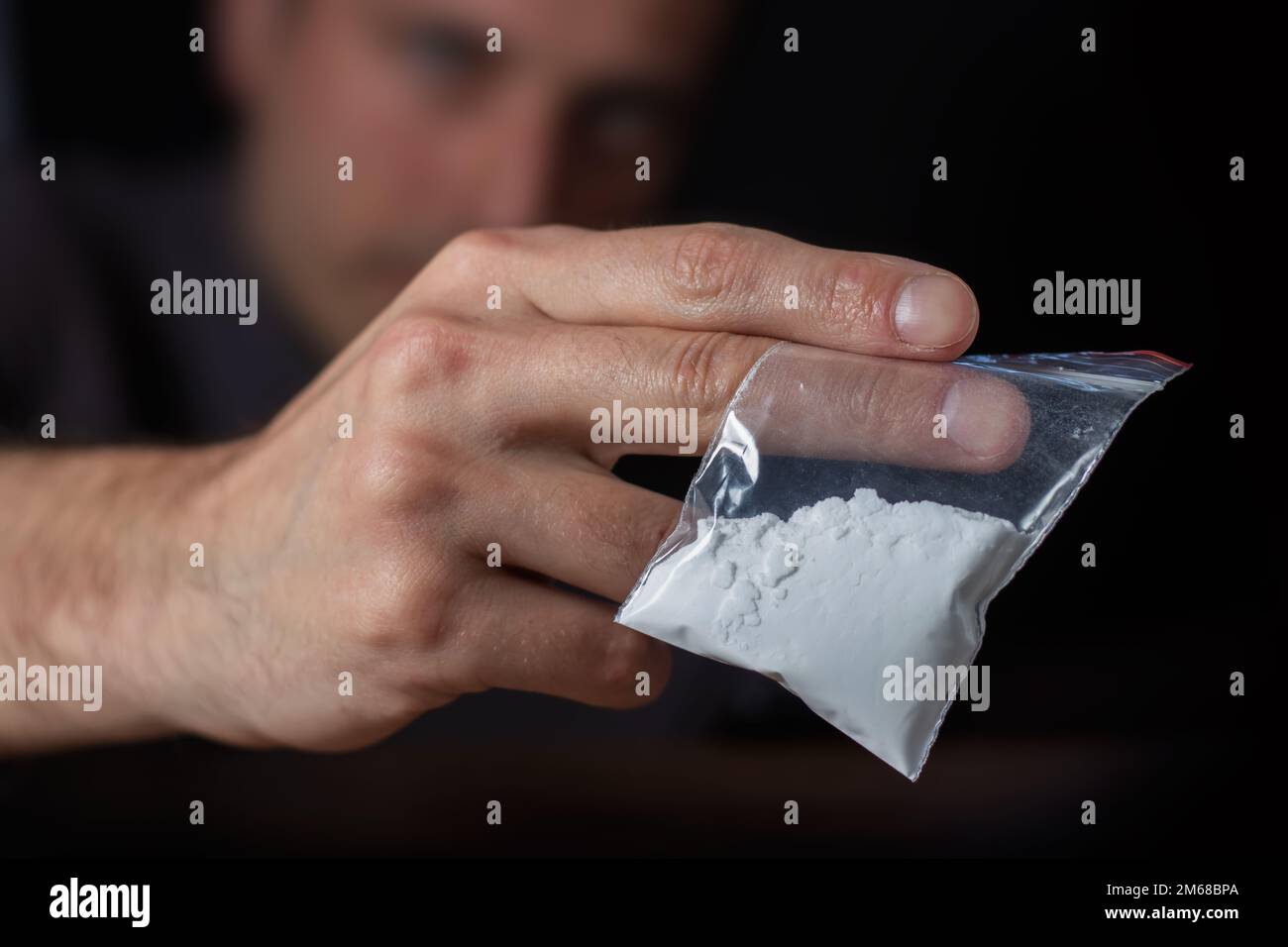 Concetto di tossicodipendenza. La mano dell'uomo tiene il pacchetto o il sacchetto di plastica con la cocaina o altre droghe, l'abuso della droga e il concetto di dipendenza di pericolo. Foto Stock